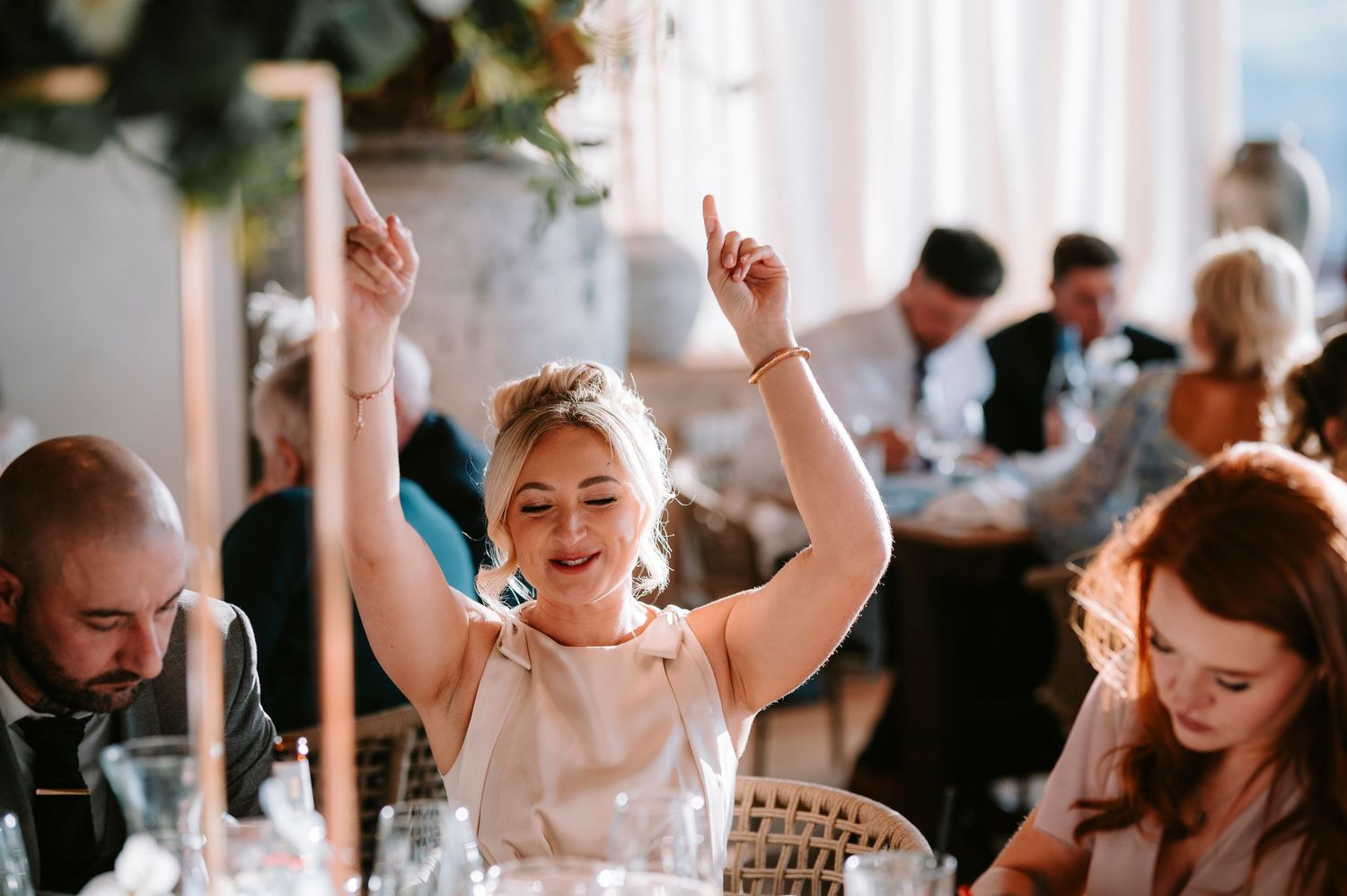 Wedding reception guests celebrate with raised hands and joyful expressions indoors.