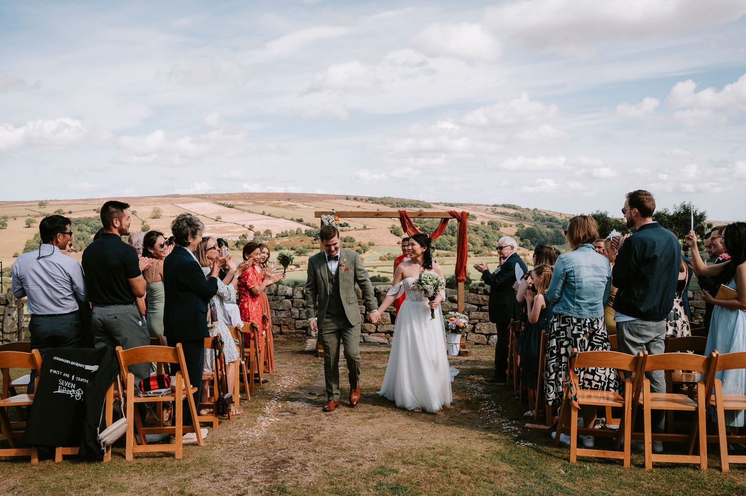 Scenic outdoor wedding ceremony with guests seated on wooden chairs against desert landscape backdrop.