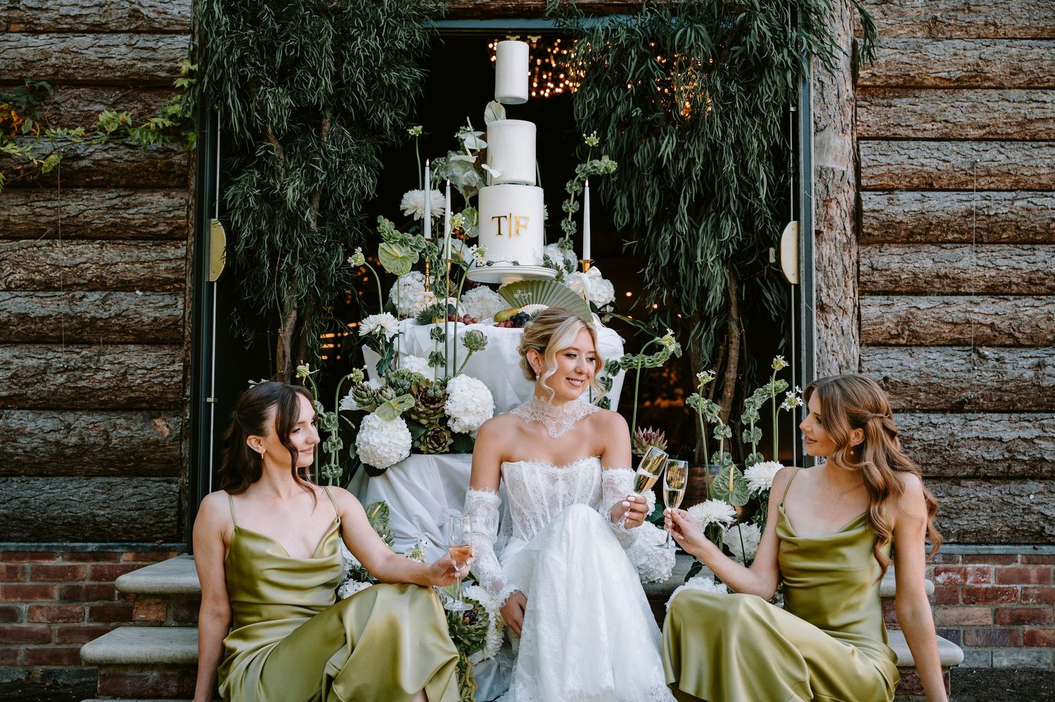 Bridesmaids in sage green dresses holding white floral bouquets pose with bride in rustic cabin setting.
