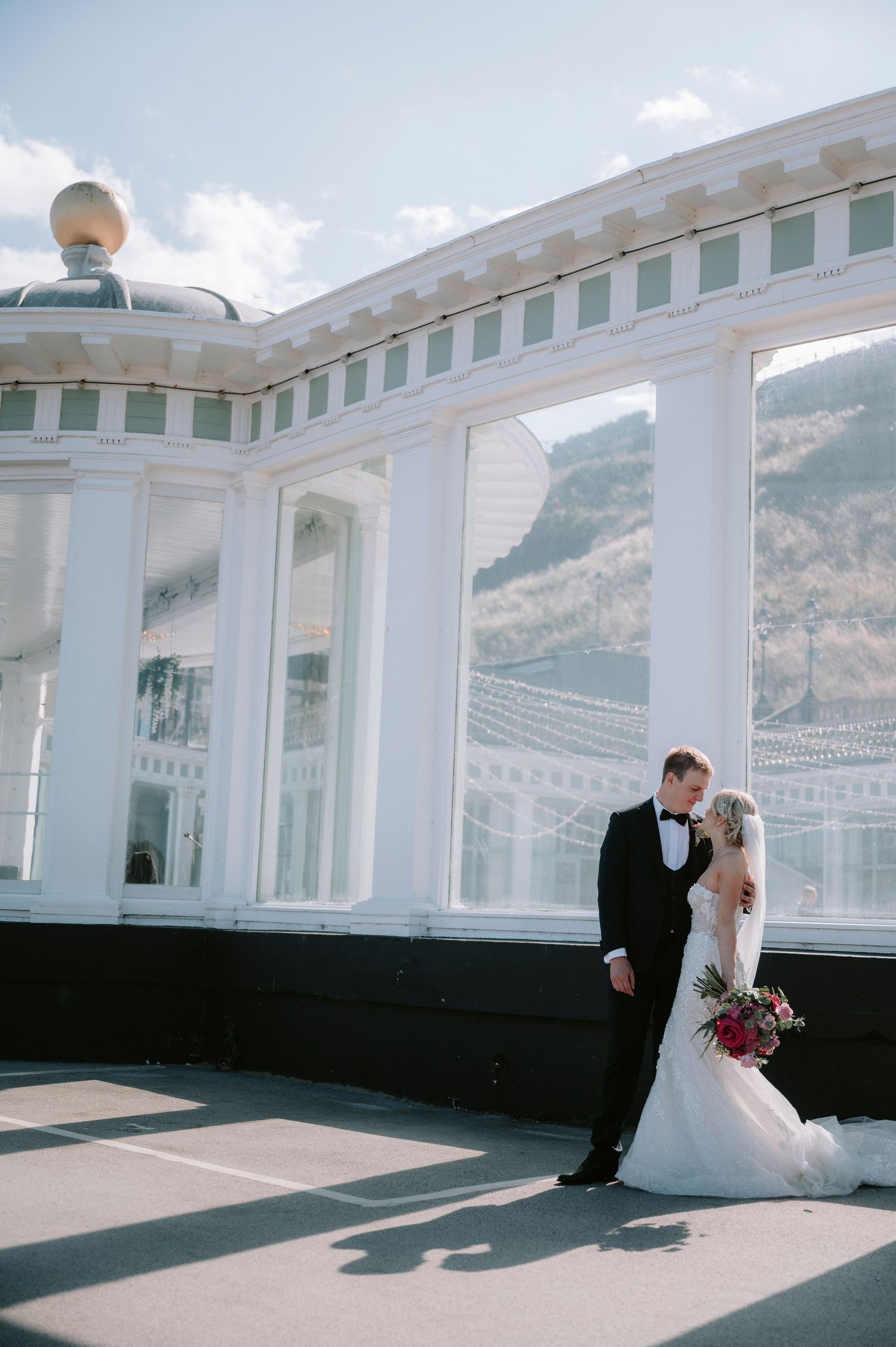 Couple shares intimate moment against architectural backdrop with dramatic lighting and shadows.