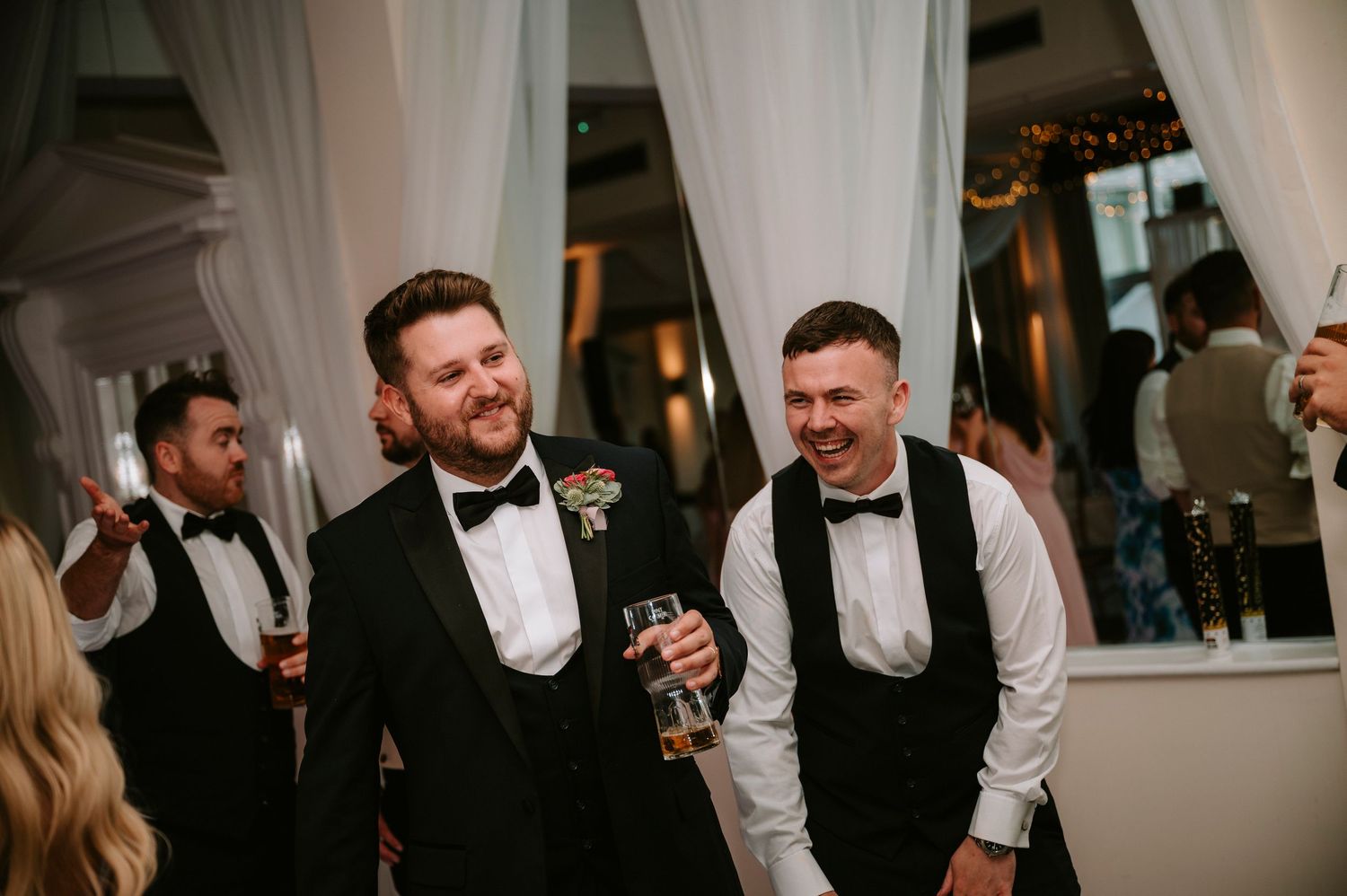Groomsmen in black tuxedos socializing during the wedding reception.