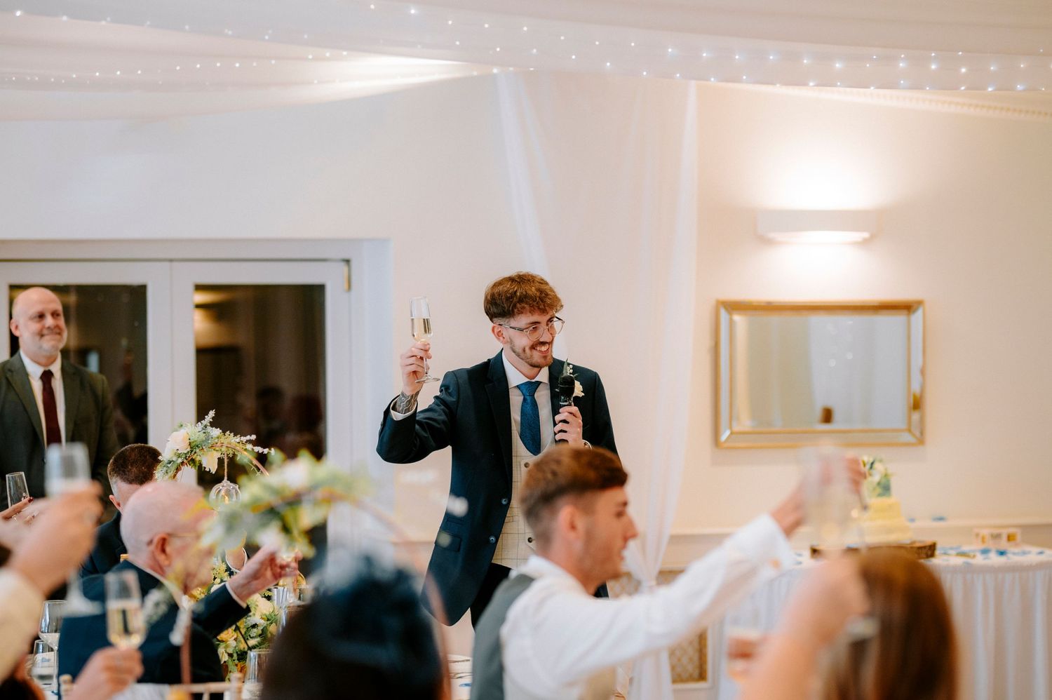 Wedding guests reacting with laughter and raised hands during reception speeches.
