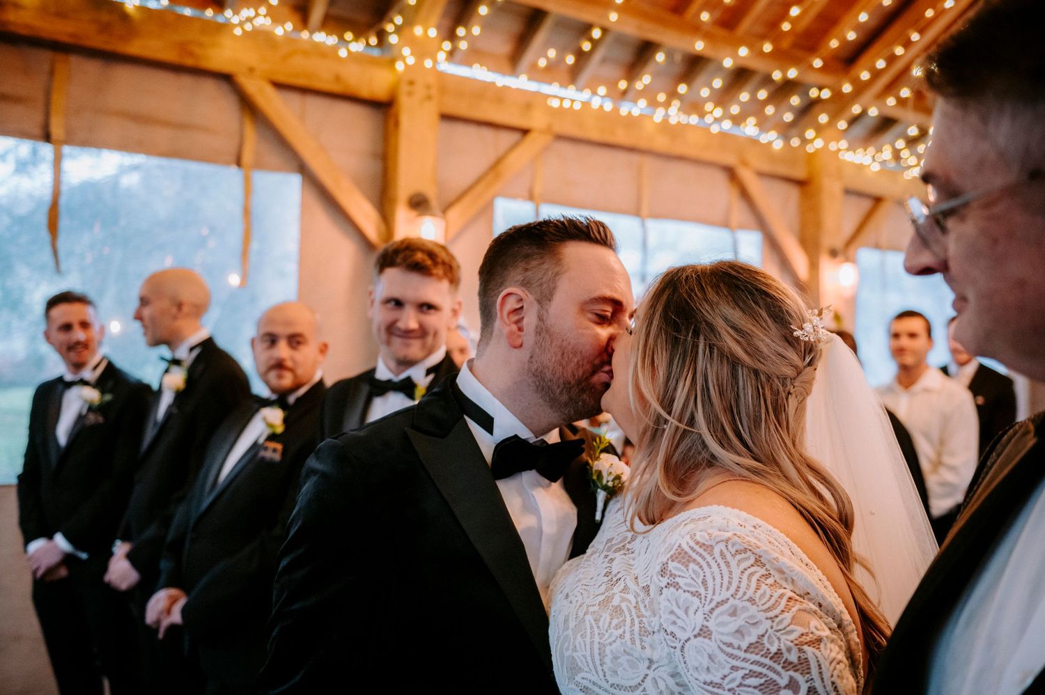 An intimate wedding ceremony moment in a rustic barn venue with twinkling lights overhead.