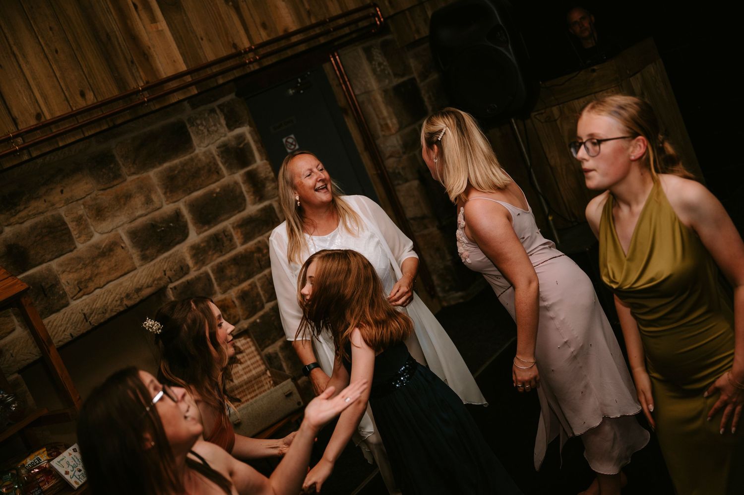 People dancing and having fun at a dimly lit party venue with wooden beams visible overhead.