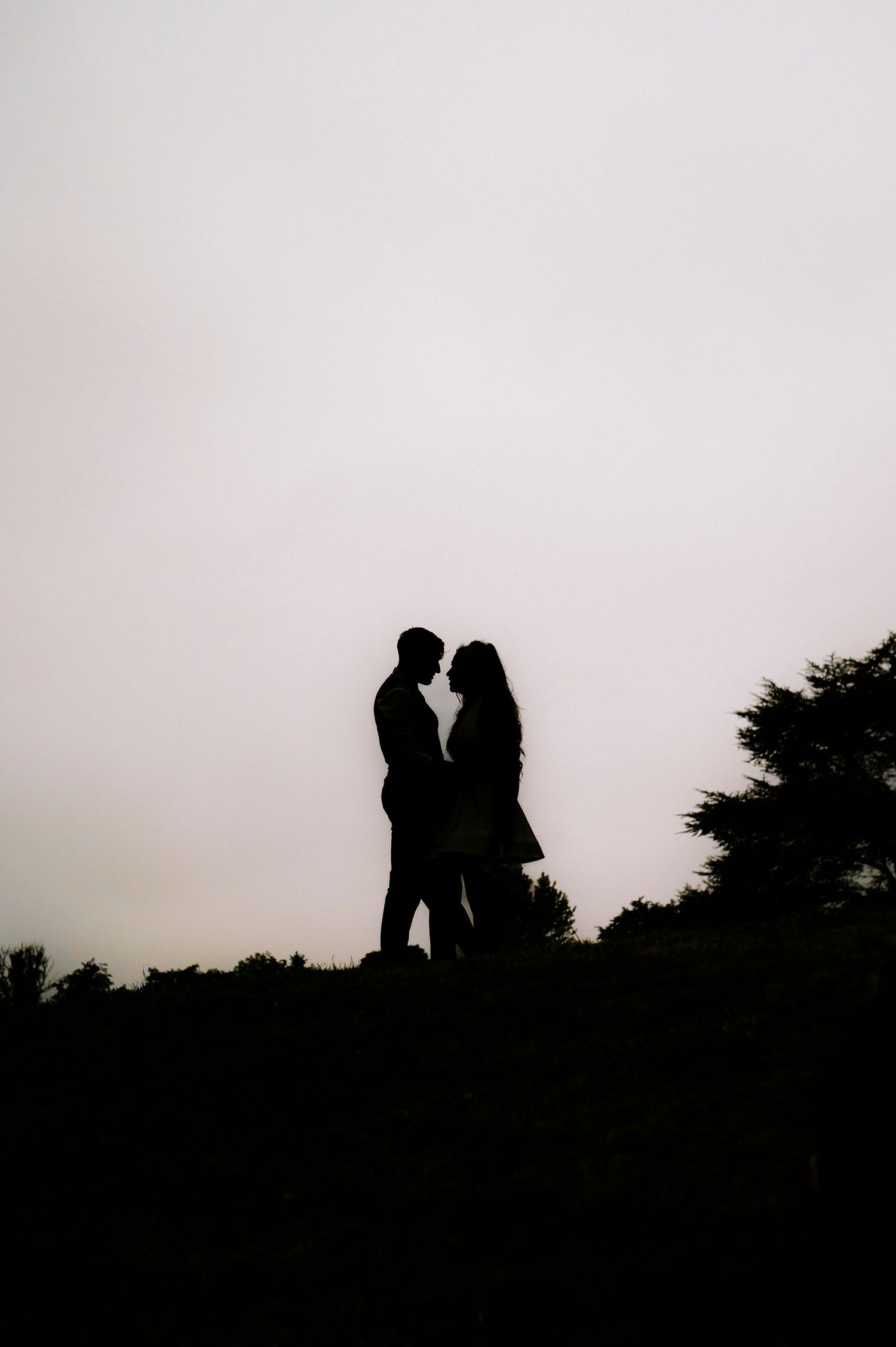Silhouettes of a couple against a misty sky during sunset.