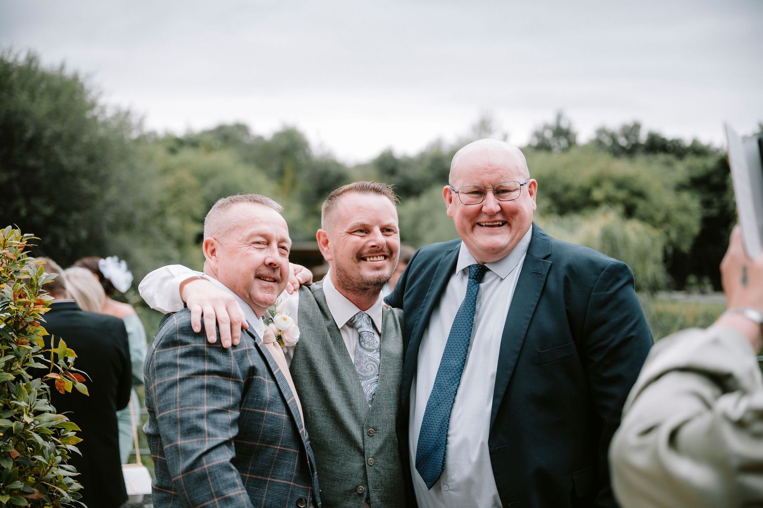 Wedding guests in formal attire sharing laughs during an outdoor gathering.