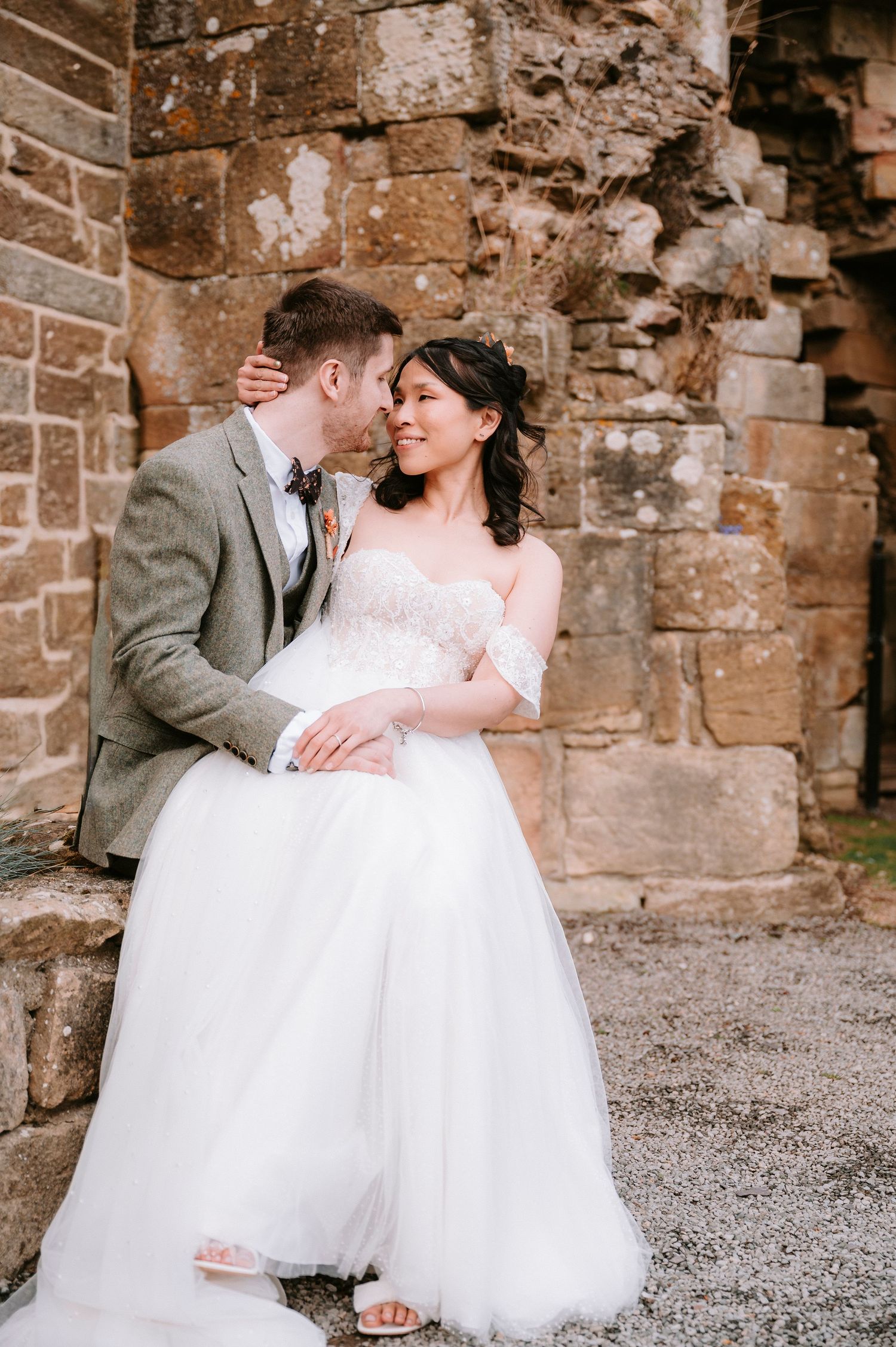 Romantic wedding couple dancing and embracing against rustic stone wall backdrop.