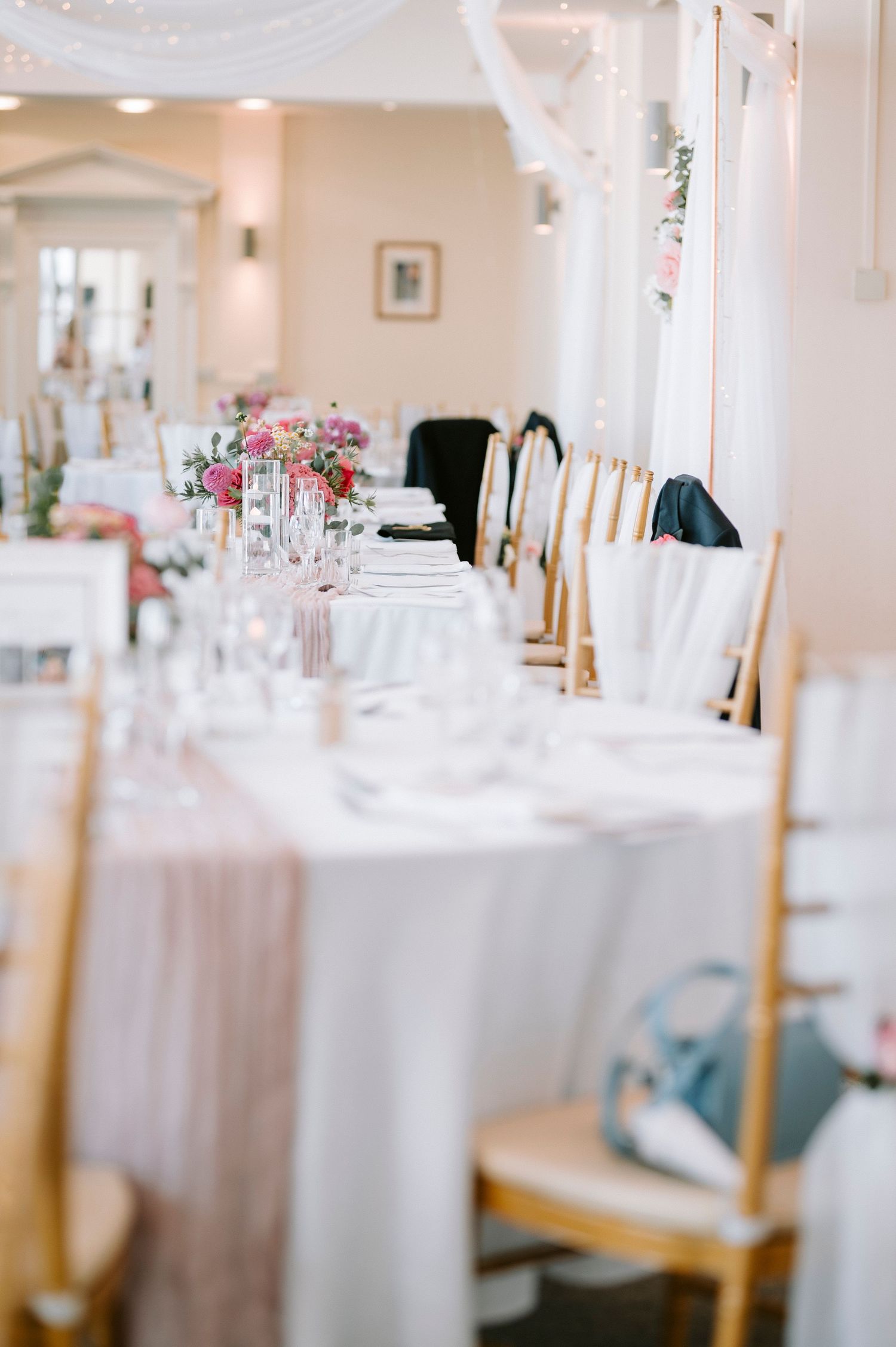 Elegant wedding reception venue with white tablecloths, gold chairs, and soft lighting creating a romantic atmosphere.