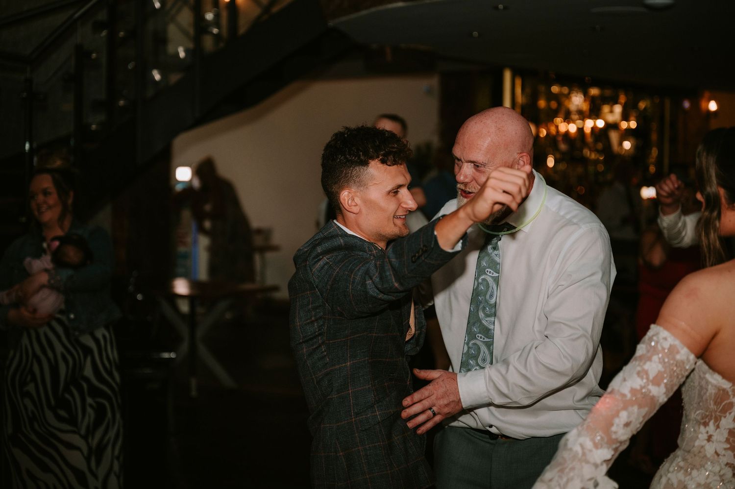 Wedding guests dancing and celebrating on a dimly lit dance floor during an evening reception.