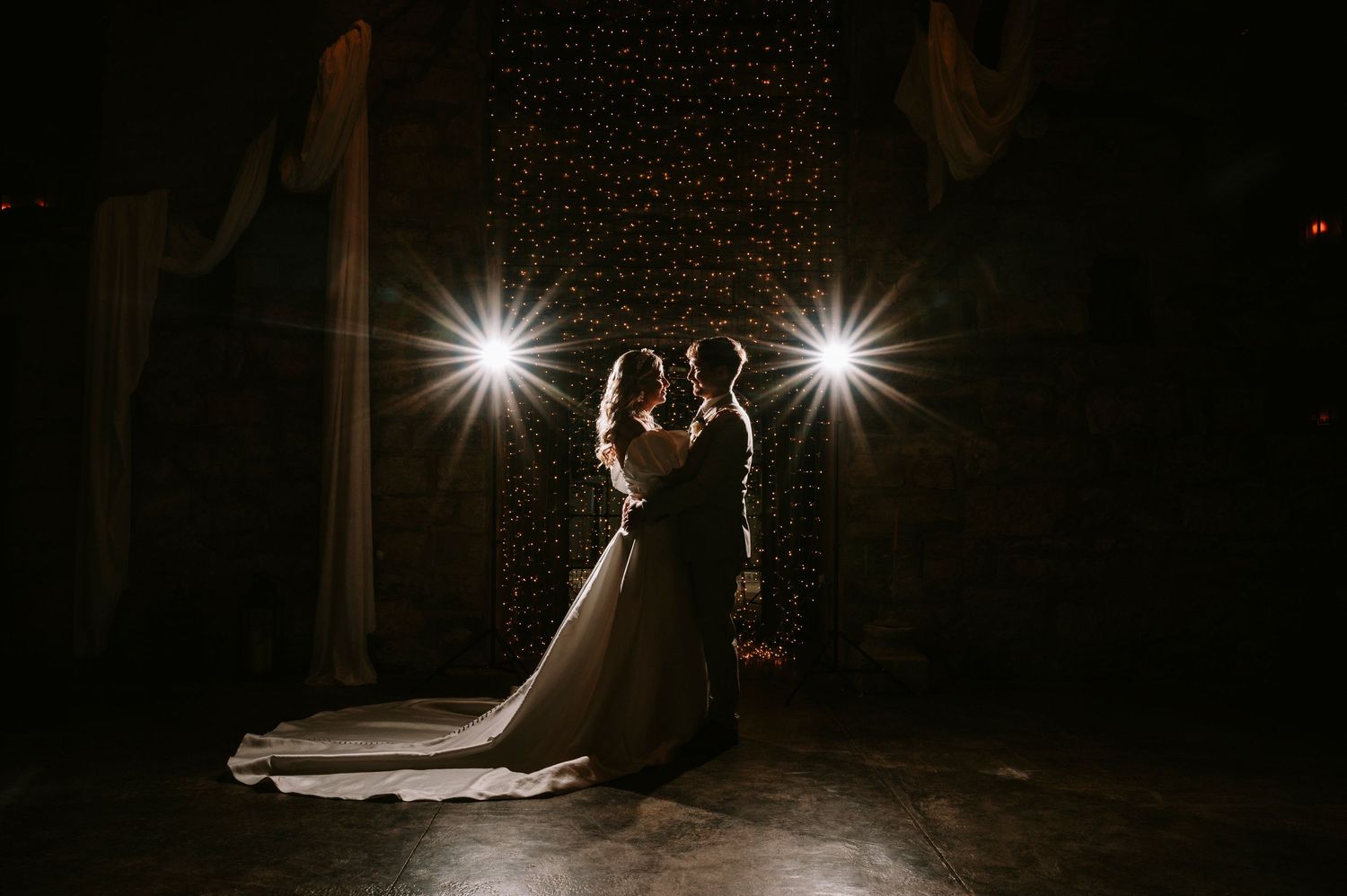 Silhouetted couple dancing in dramatic spotlight against dark background creating romantic wedding moment.