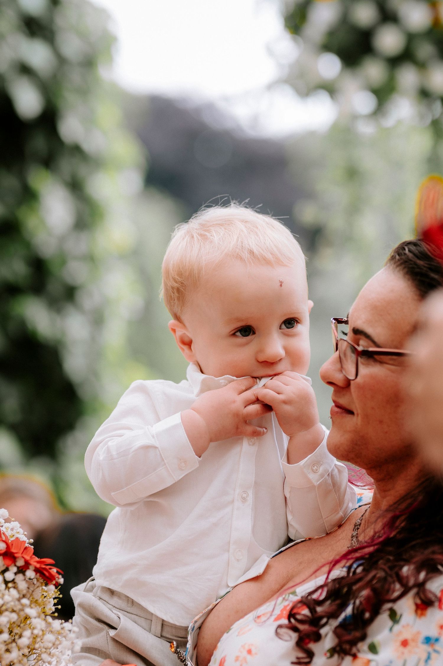 Baby in white outfit shares tender moment during outdoor celebration.