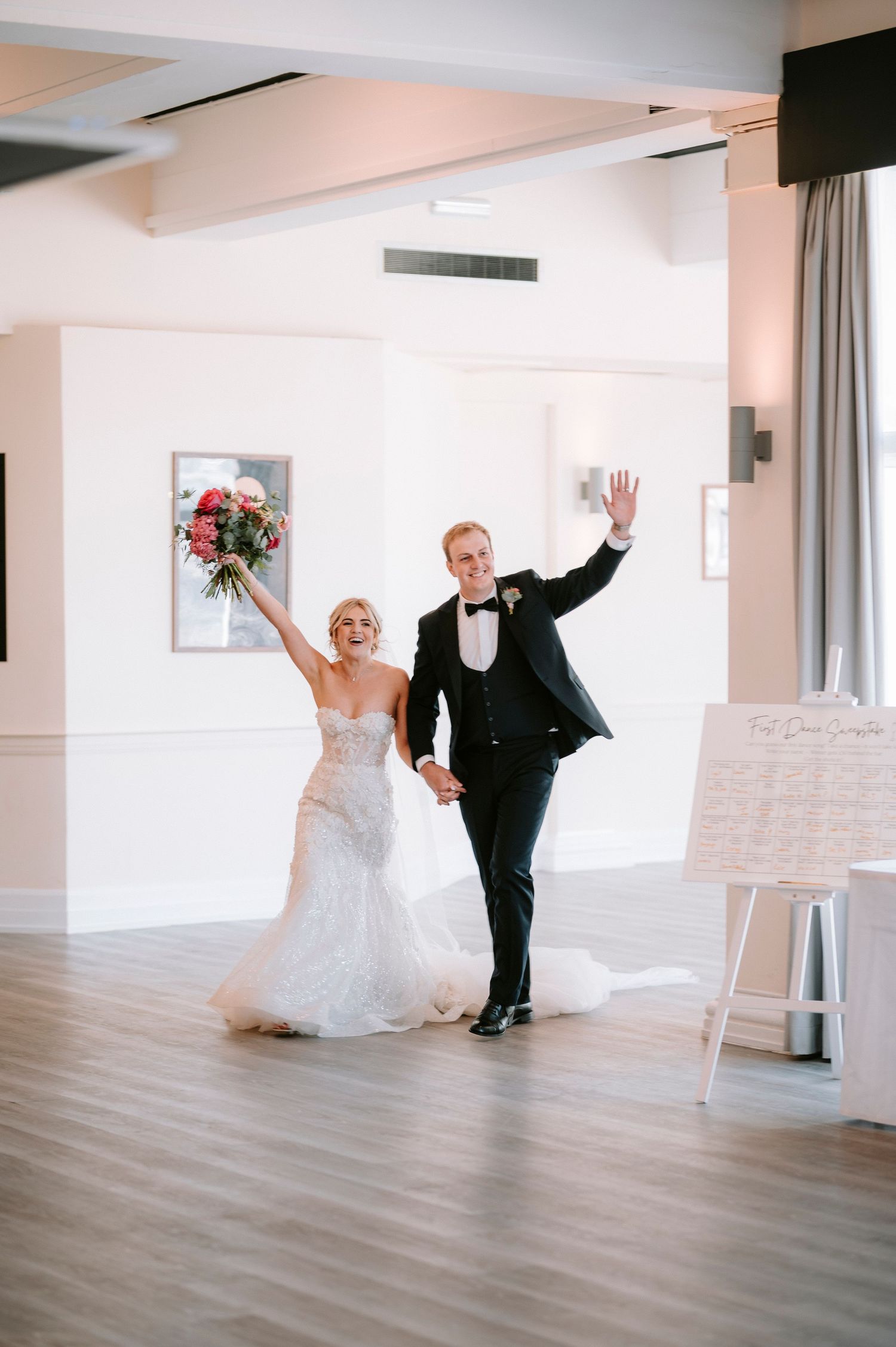 Newlyweds make grand entrance into reception hall with raised arms and flowers.