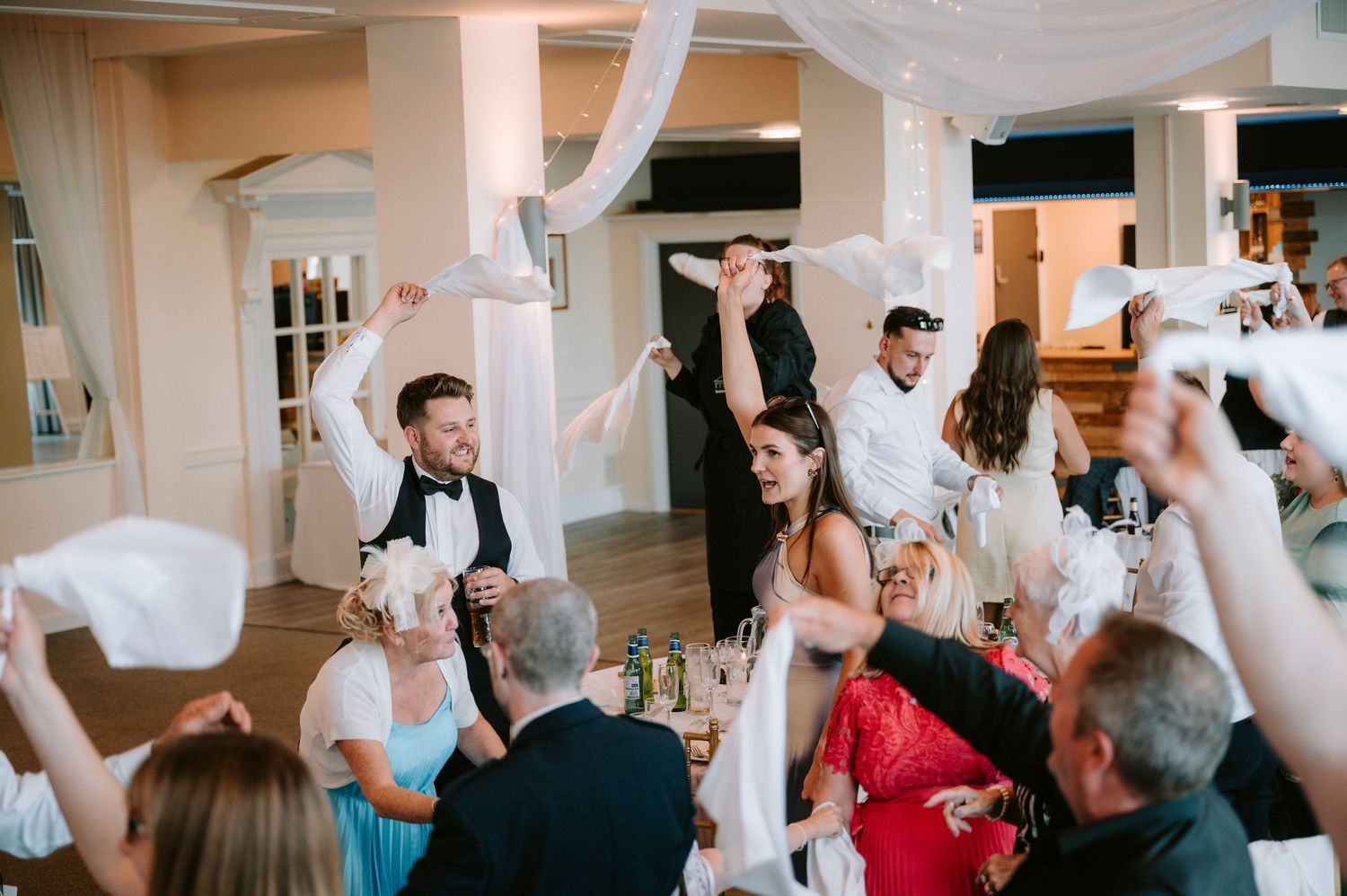 Wedding reception guests wave napkins in unison during a festive celebration moment.