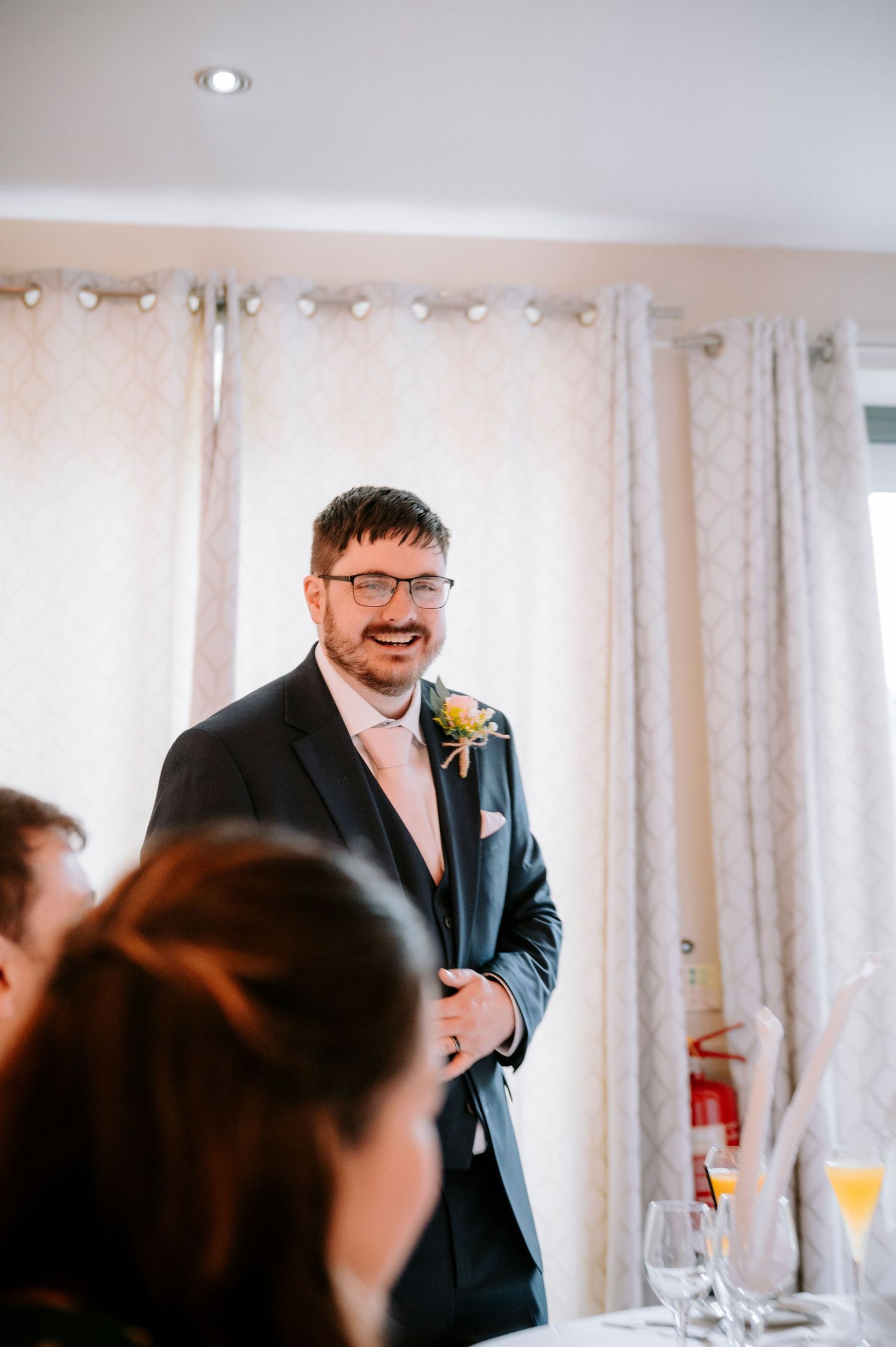 Wedding reception guests enjoy drinks and conversation in an indoor venue with white curtains.