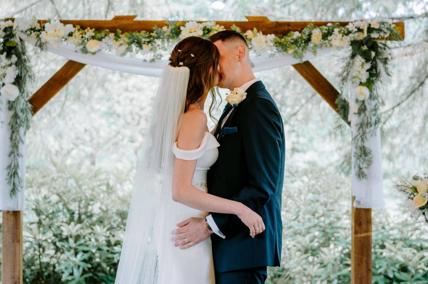 Outdoor wedding ceremony in covered pavilion surrounded by greenery.