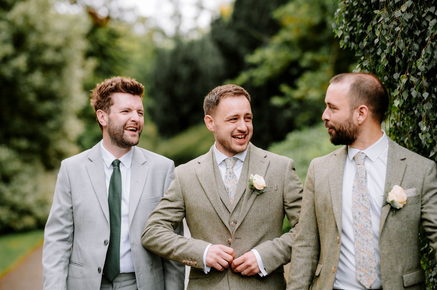 Groomsmen in grey suits share laughs during outdoor wedding photos.