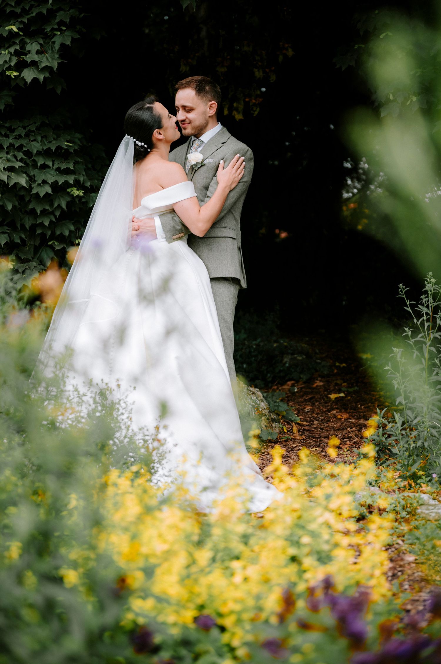 Artistic wedding portrait through garden flowers with soft focus foreground.
