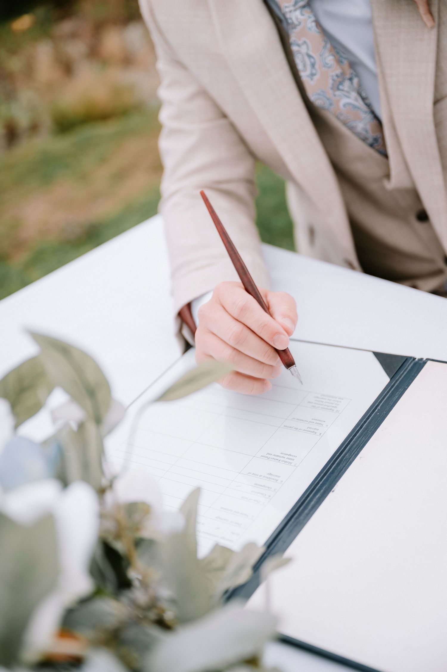 Close-up shots of hands signing wedding documents on a white tablecloth.