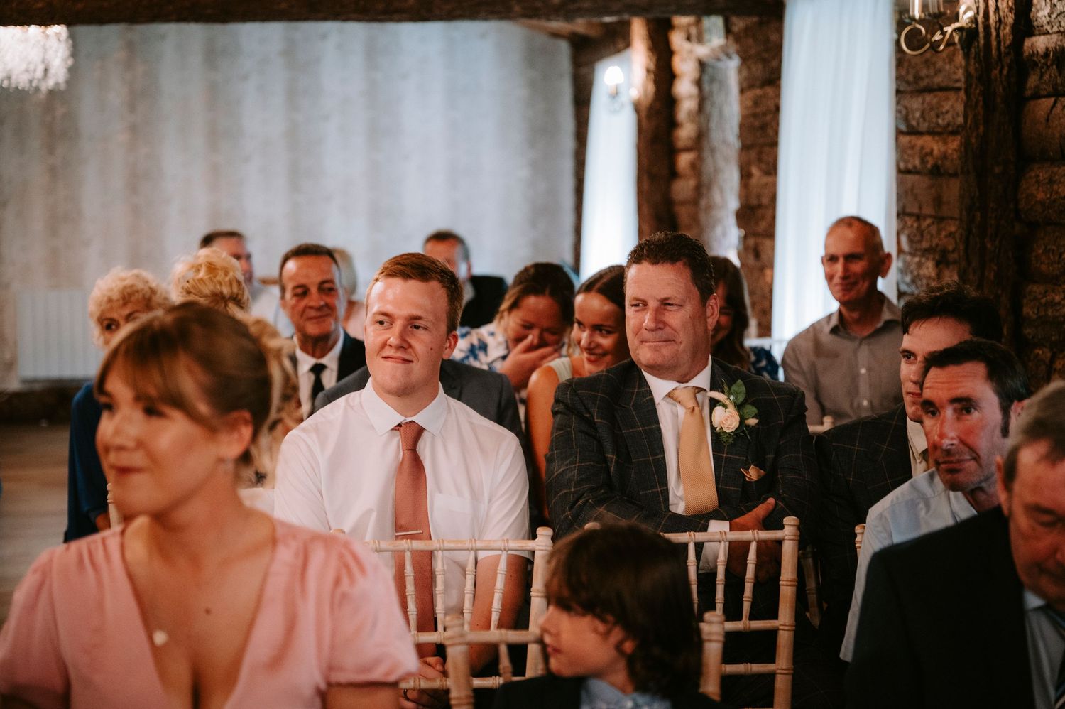 Wedding guests seated in rows during ceremony in rustic indoor venue.