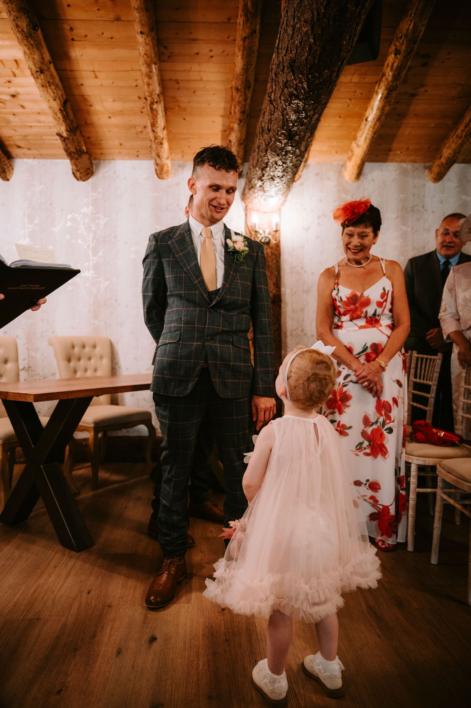 Wedding reception scene with guests in formal attire mingling on wooden floors with rustic decor.