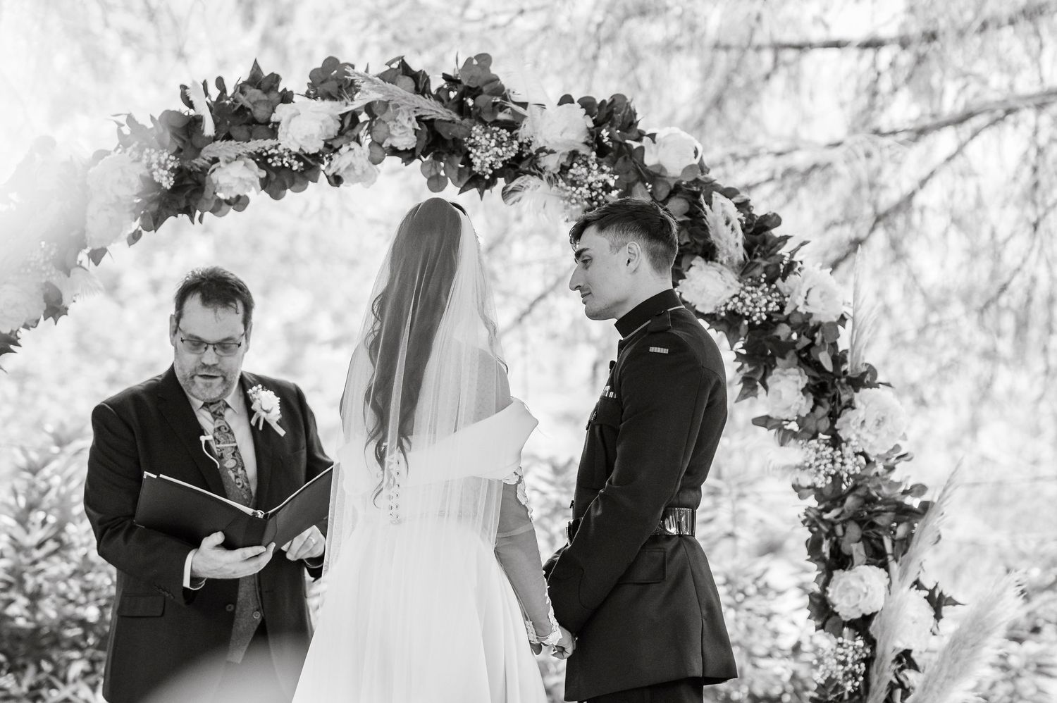 Wedding ceremony setup with floral arch and chairs in an outdoor forest setting.