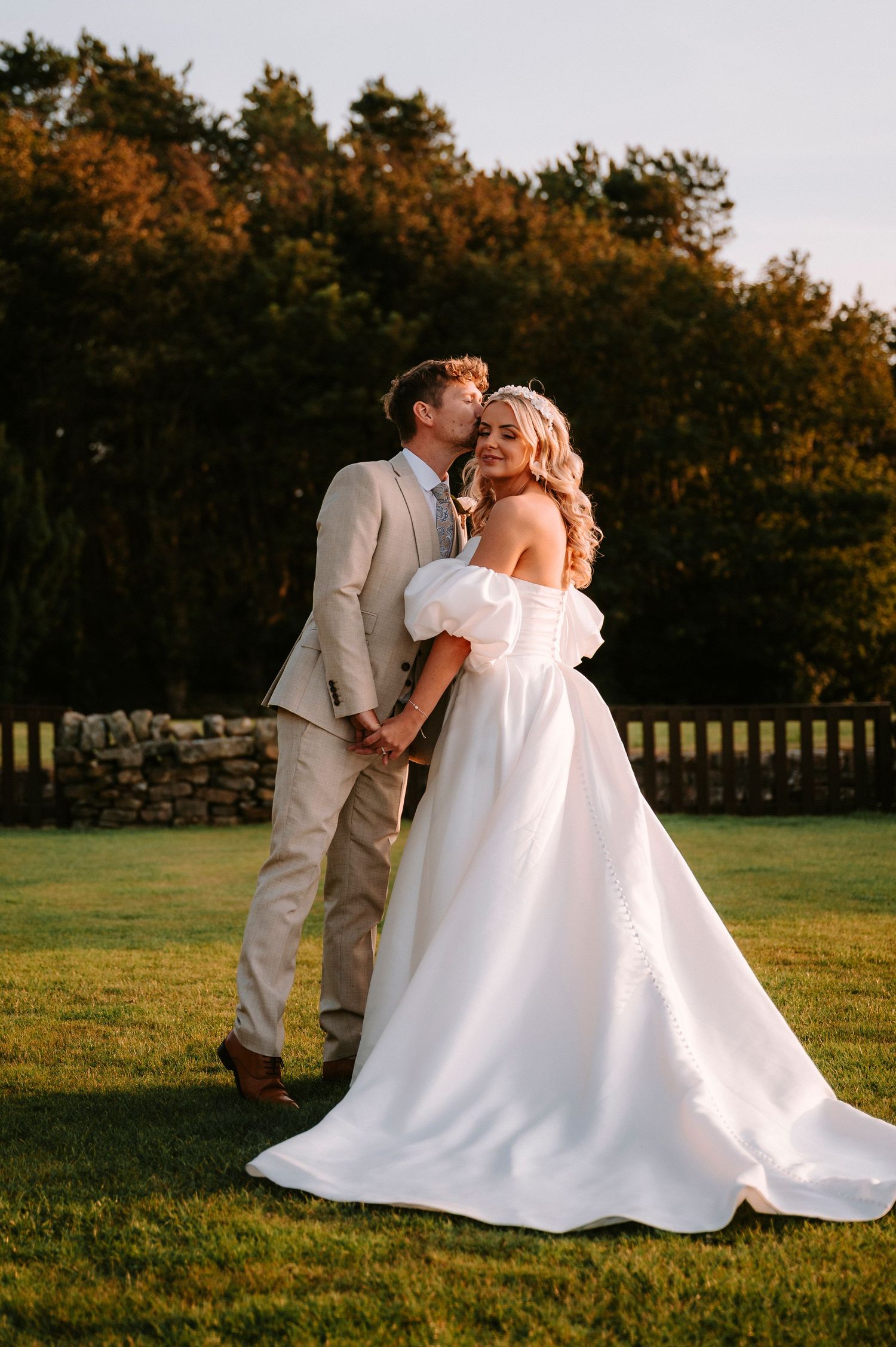 Romantic sunset portrait of newlyweds on a grassy lawn with autumn trees in background.