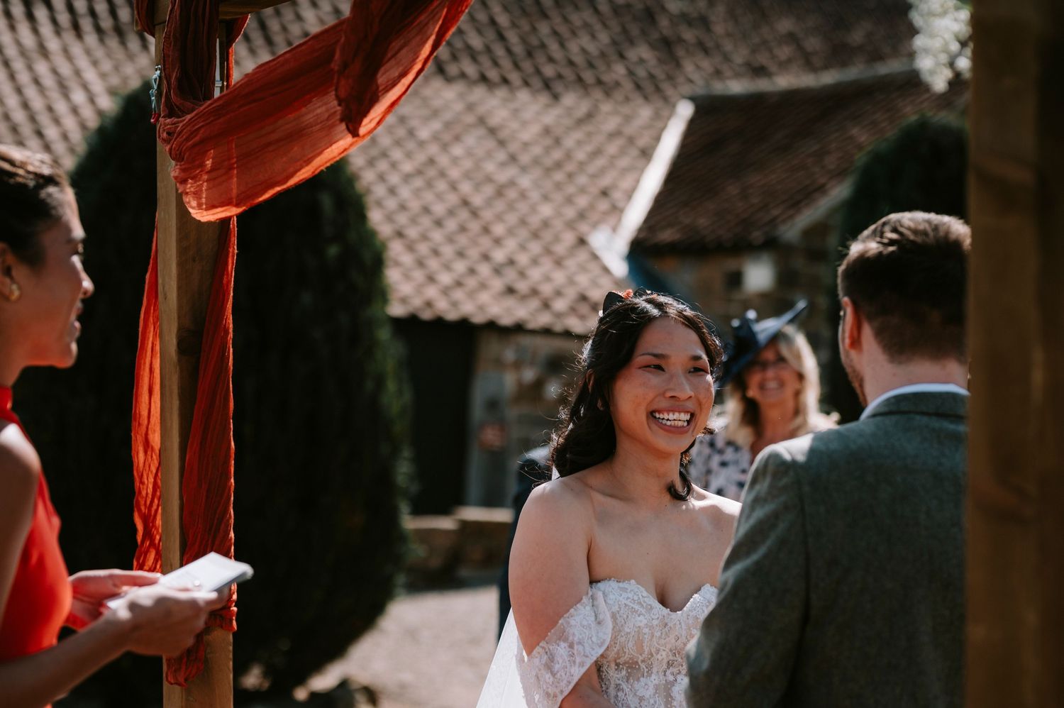 Wedding ceremony taking place under rustic wooden beams with red fabric draping.