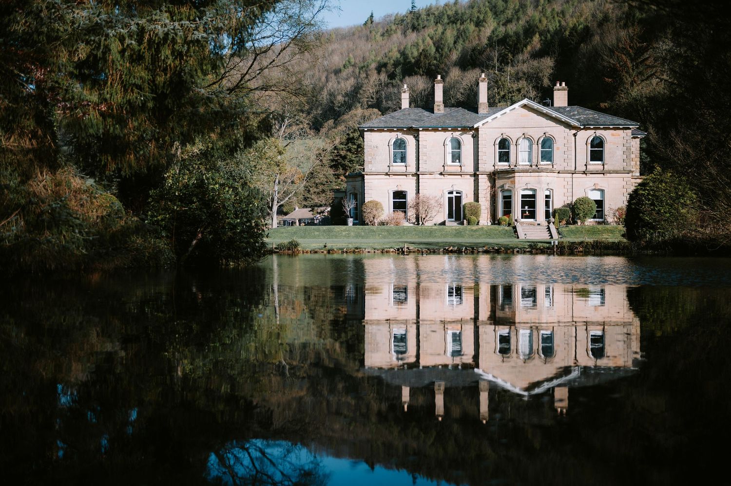 Historic pink manor house reflects beautifully in still water on a sunny day.
