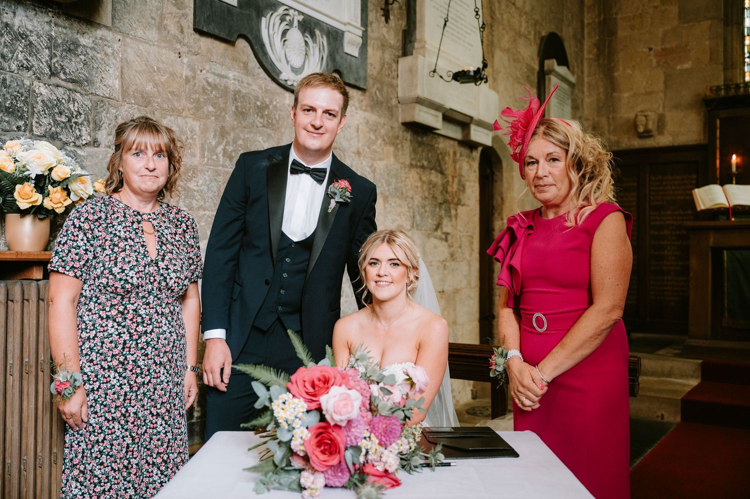 Wedding guests in formal attire gathered in a historic church with pink floral decorations.