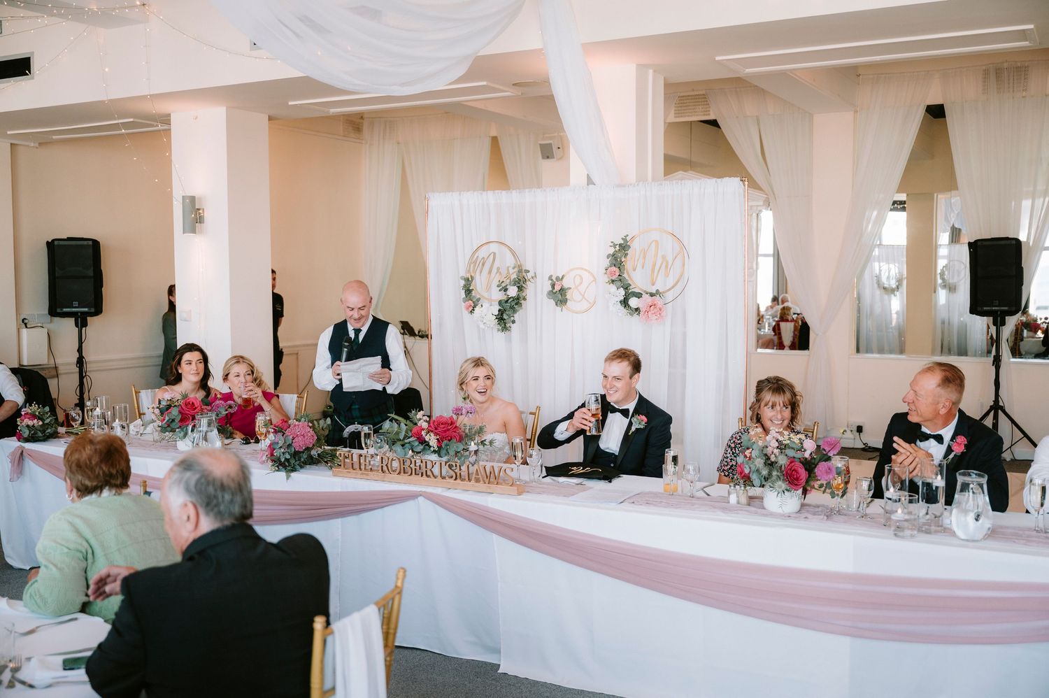 Wedding reception setup with head table decorated in pink and white linens.