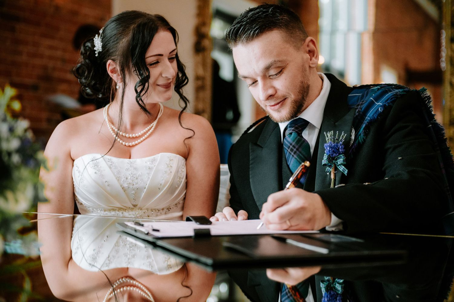 Newlyweds sign their marriage documents together at a rustic venue.