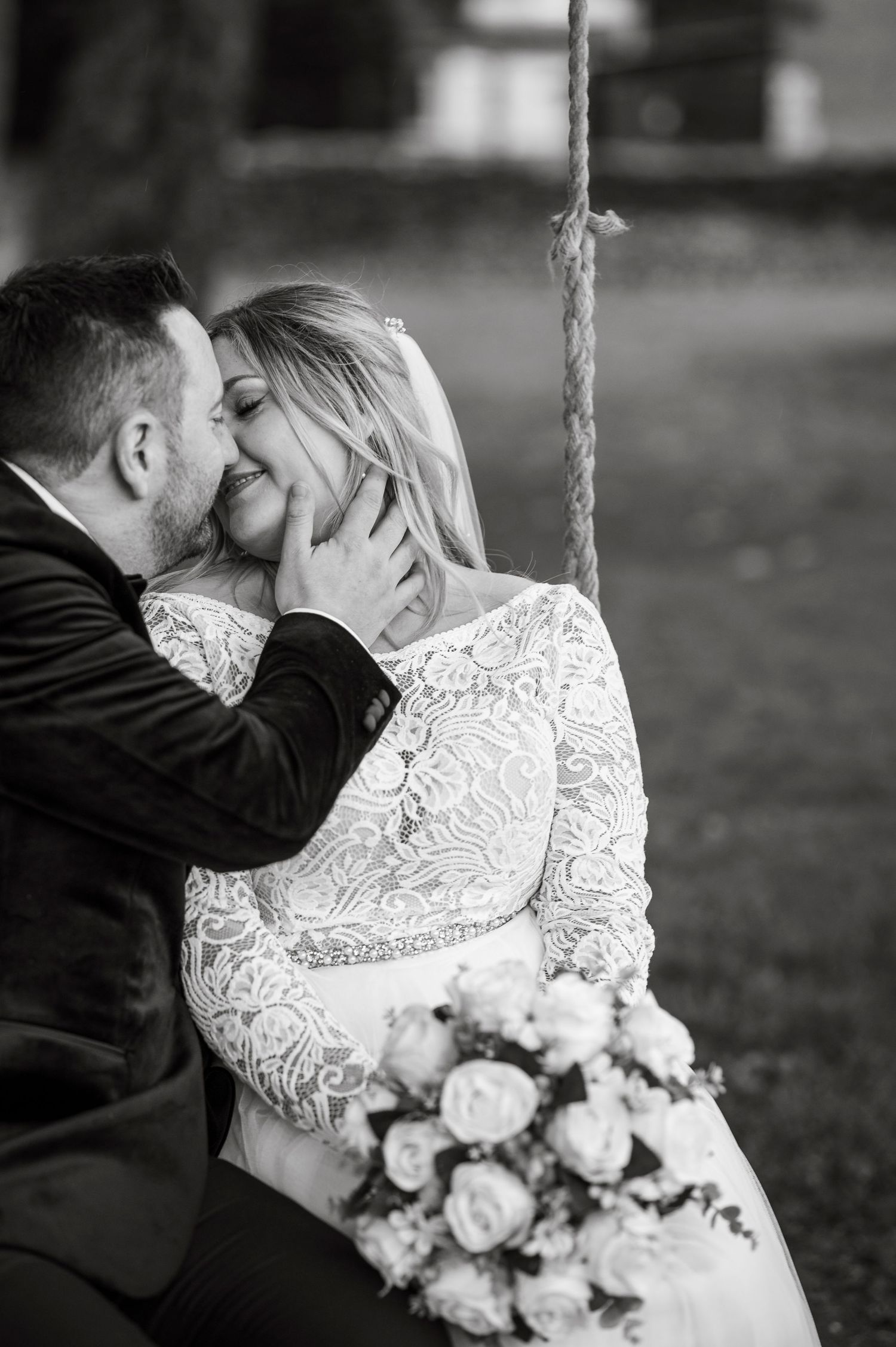 An intimate black and white portrait of newlyweds sharing a tender moment on a swing.