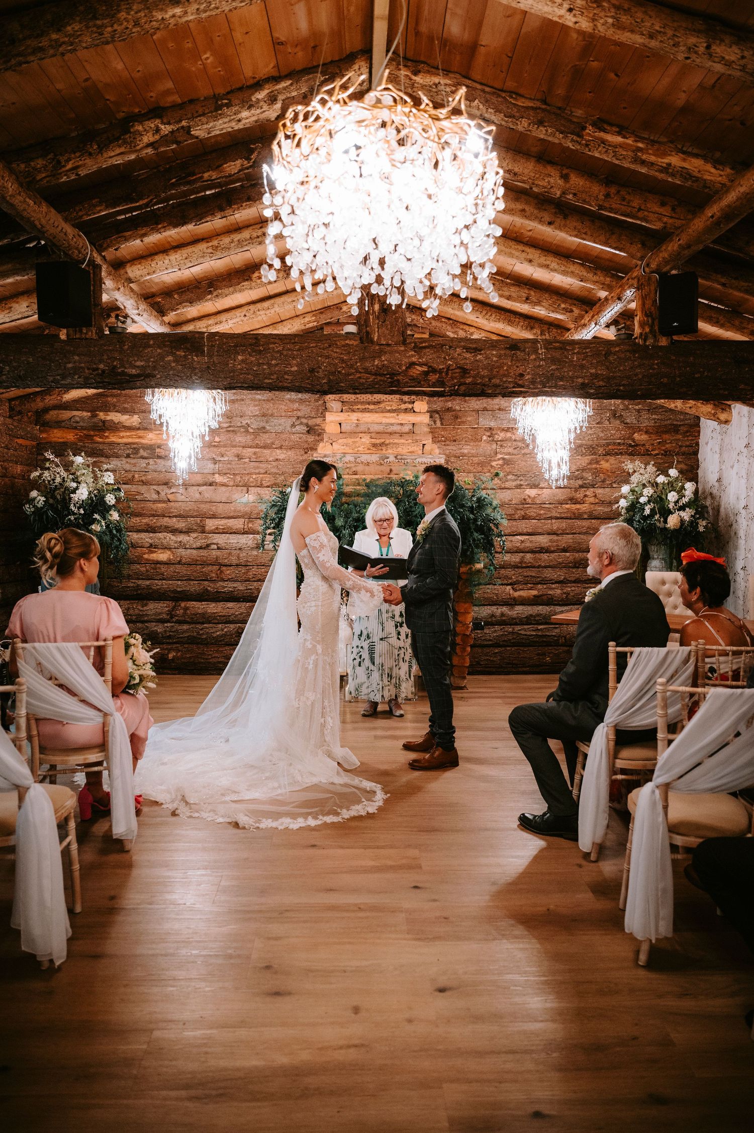 Wedding ceremony in a rustic barn venue with wooden beams and elegant crystal chandeliers.