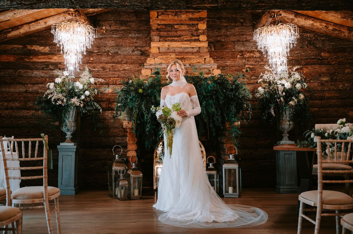 Elegant wedding scene with cascading lights, greenery and floral arrangements against exposed brick wall in rustic indoor venue.