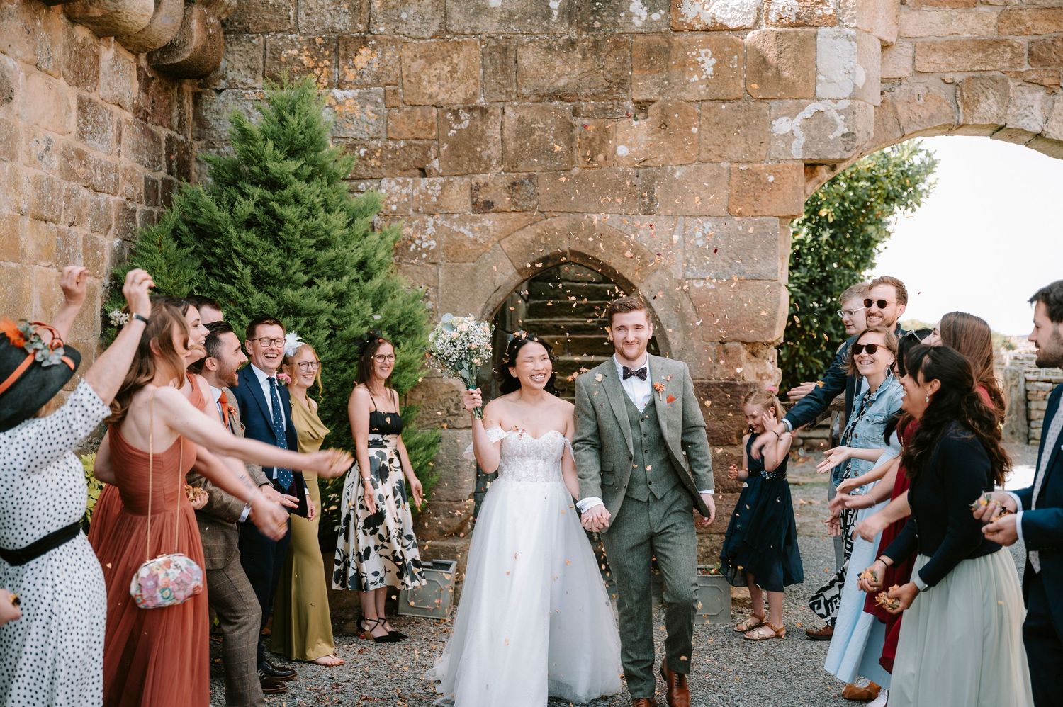 Wedding party and guests celebrating outside rustic stone venue.