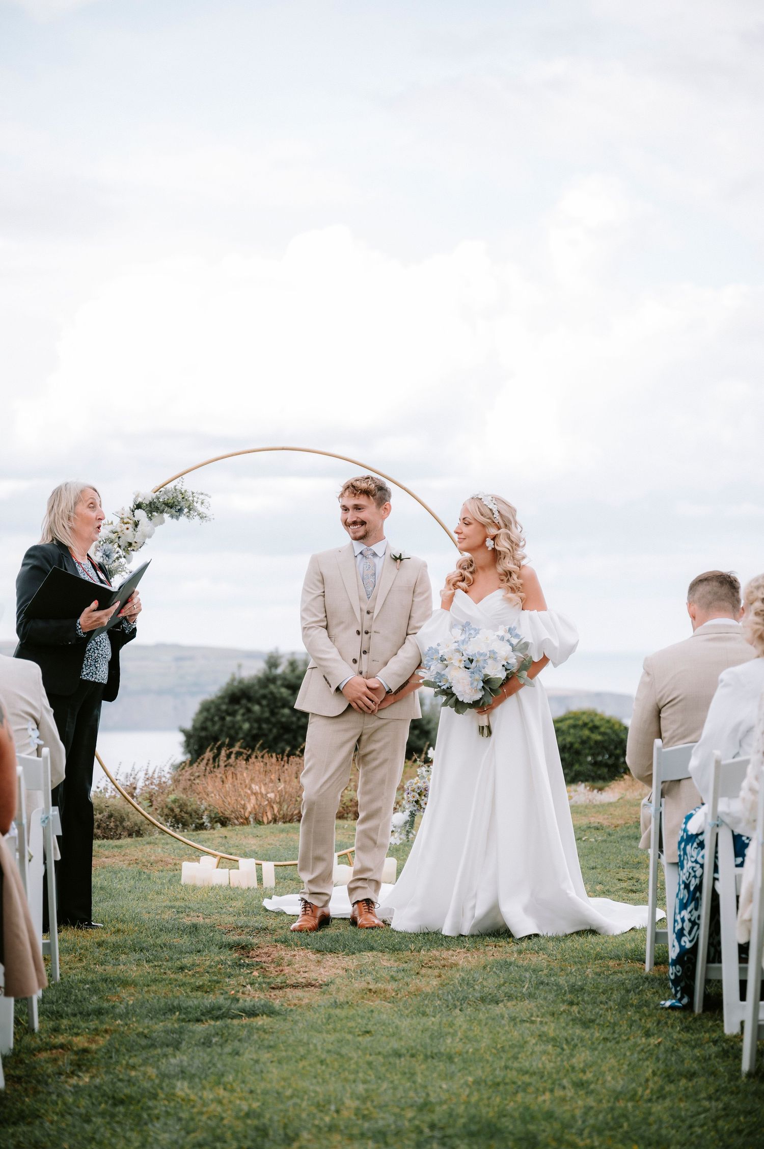 Outdoor wedding ceremony setup with white chairs and floral arch against a scenic mountain backdrop.