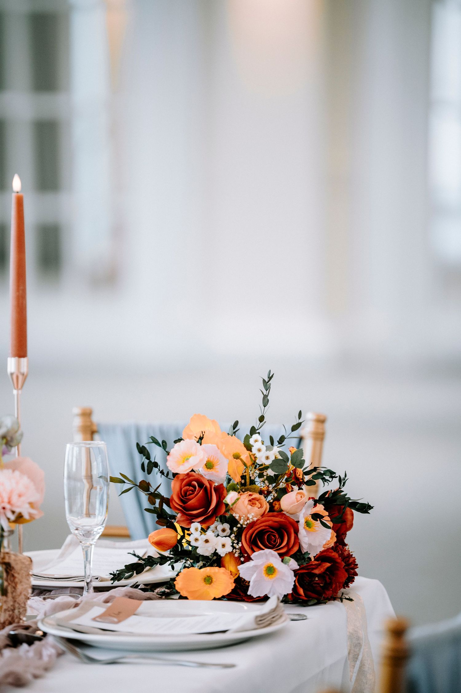 Close-up of romantic table decor with coral roses, white flowers, and tall orange candles.