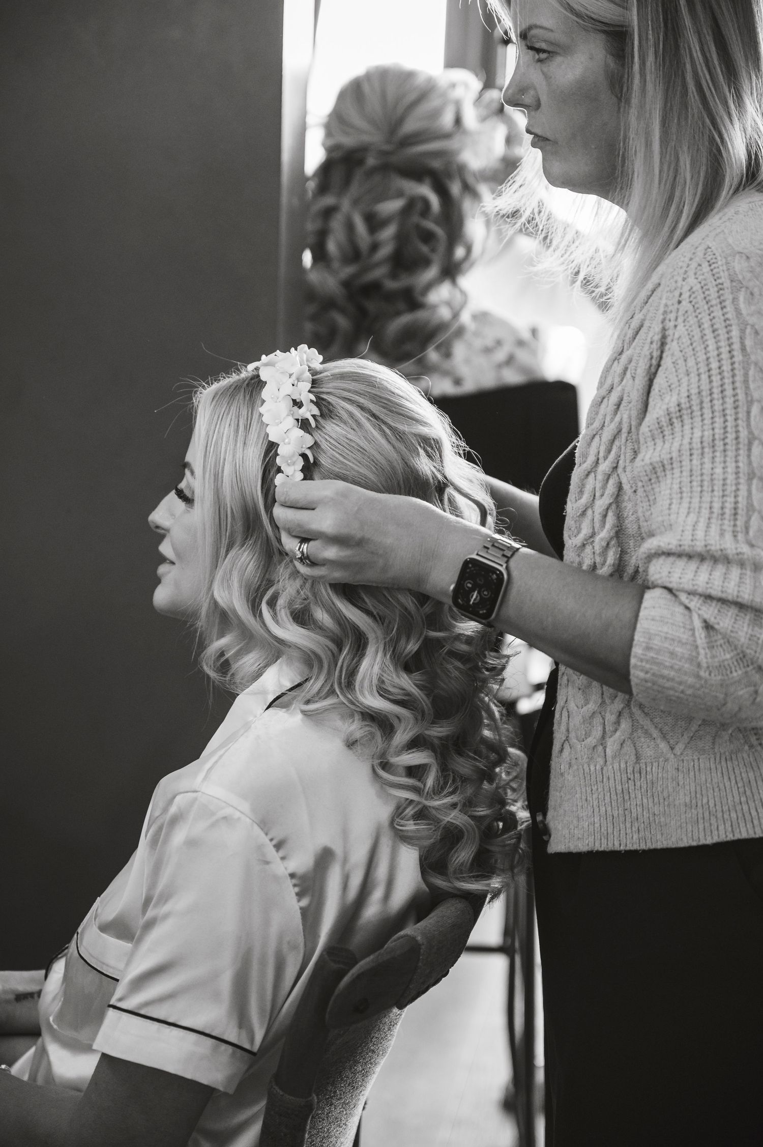 Wedding preparation scene showing hair styling with curls and floral accessories in black and white.