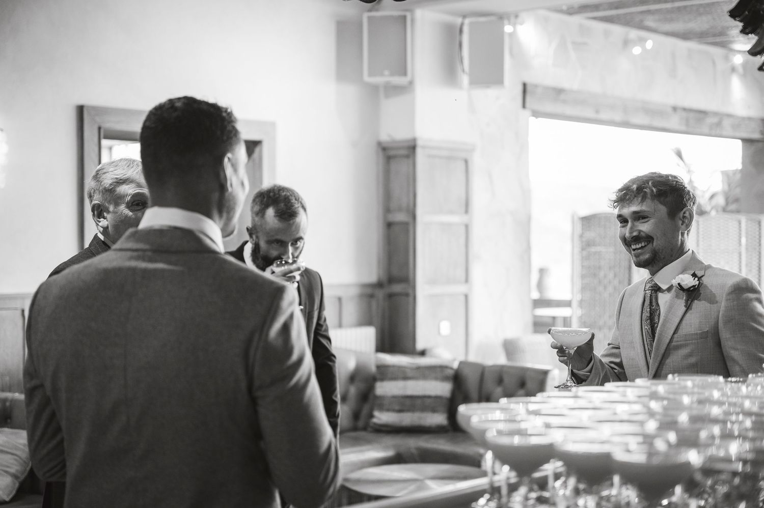 Black and white photo of groomsmen having drinks and conversation before the ceremony.