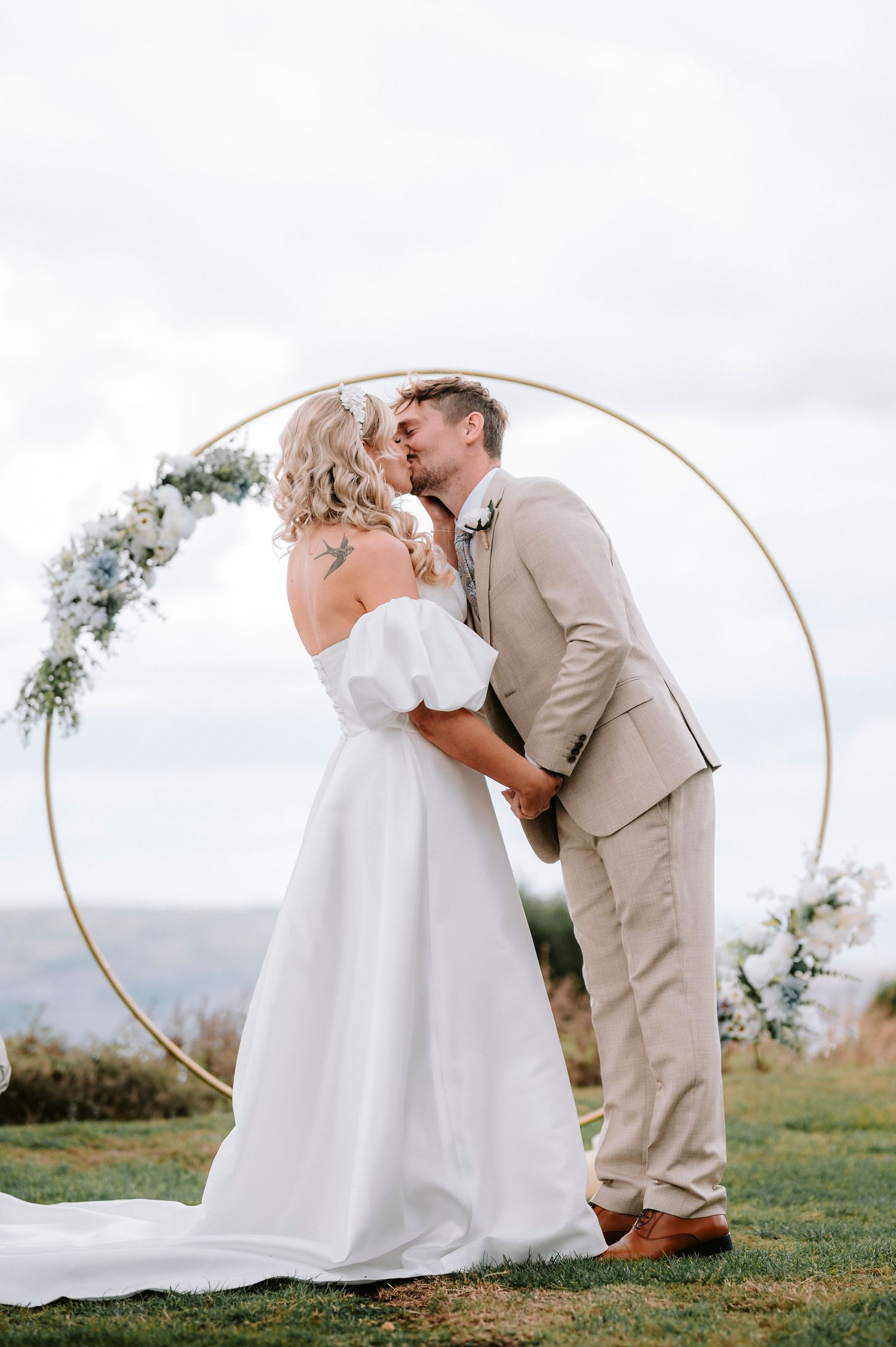 A romantic wedding photoshoot with a decorative circular arch in an outdoor field setting.