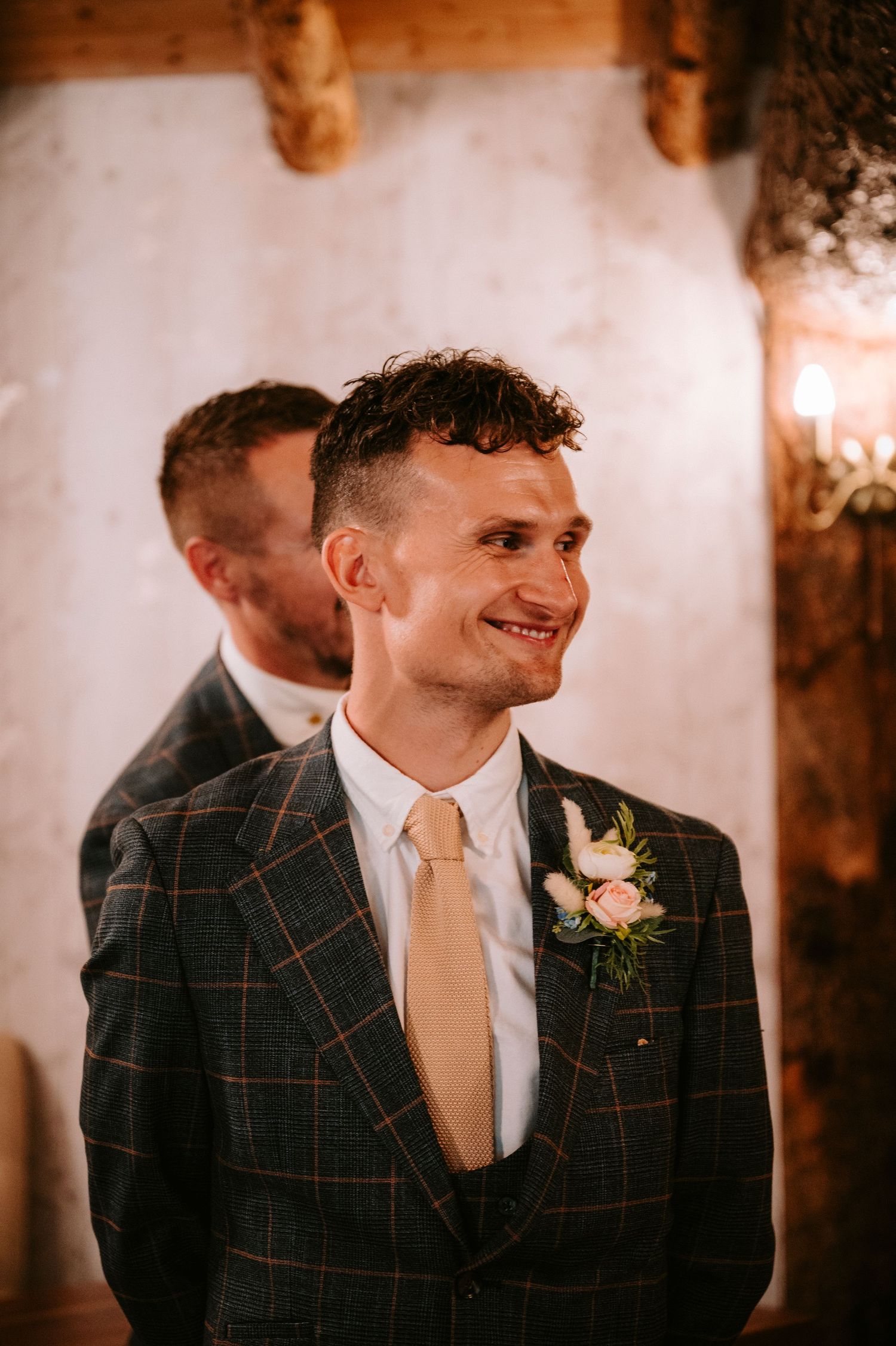 Groom wearing a plaid suit jacket with cream tie and boutonniere at a wedding reception.