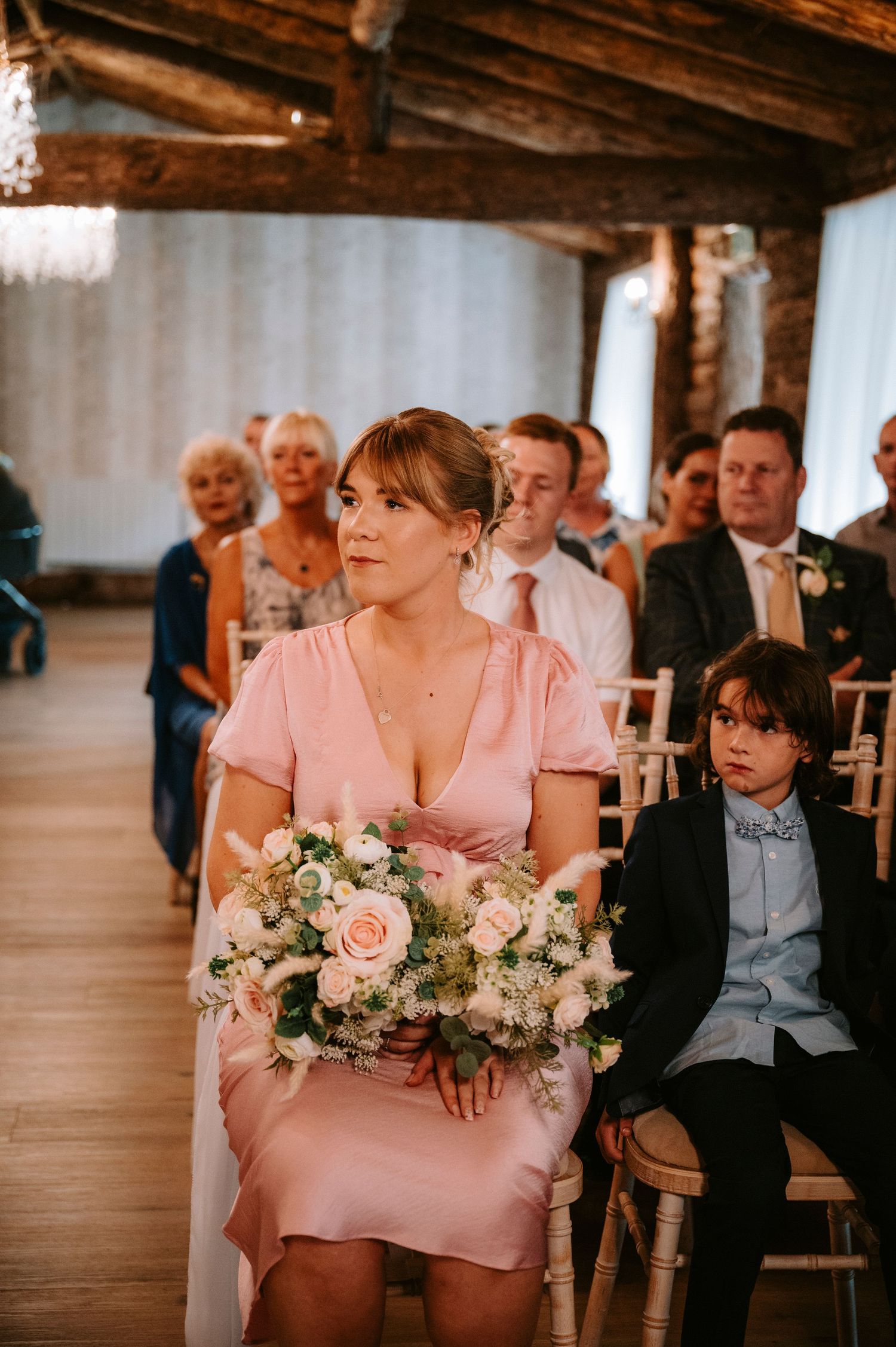 Wedding guest in pink dress holding a beautiful bouquet of roses during the ceremony.
