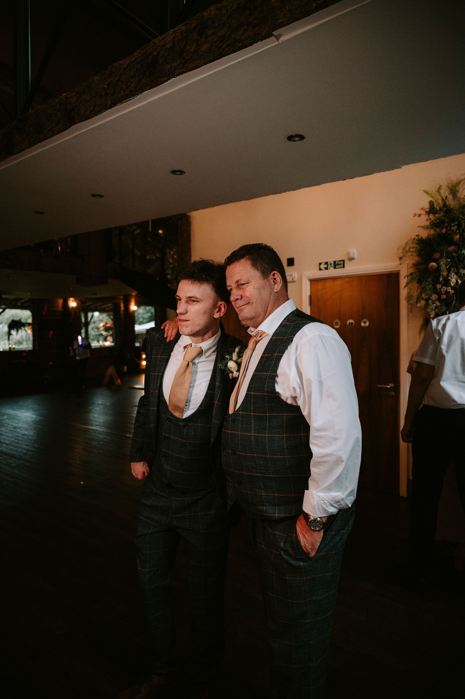 Wedding party members in formal attire sharing emotional moments during speeches at a dimly lit reception.