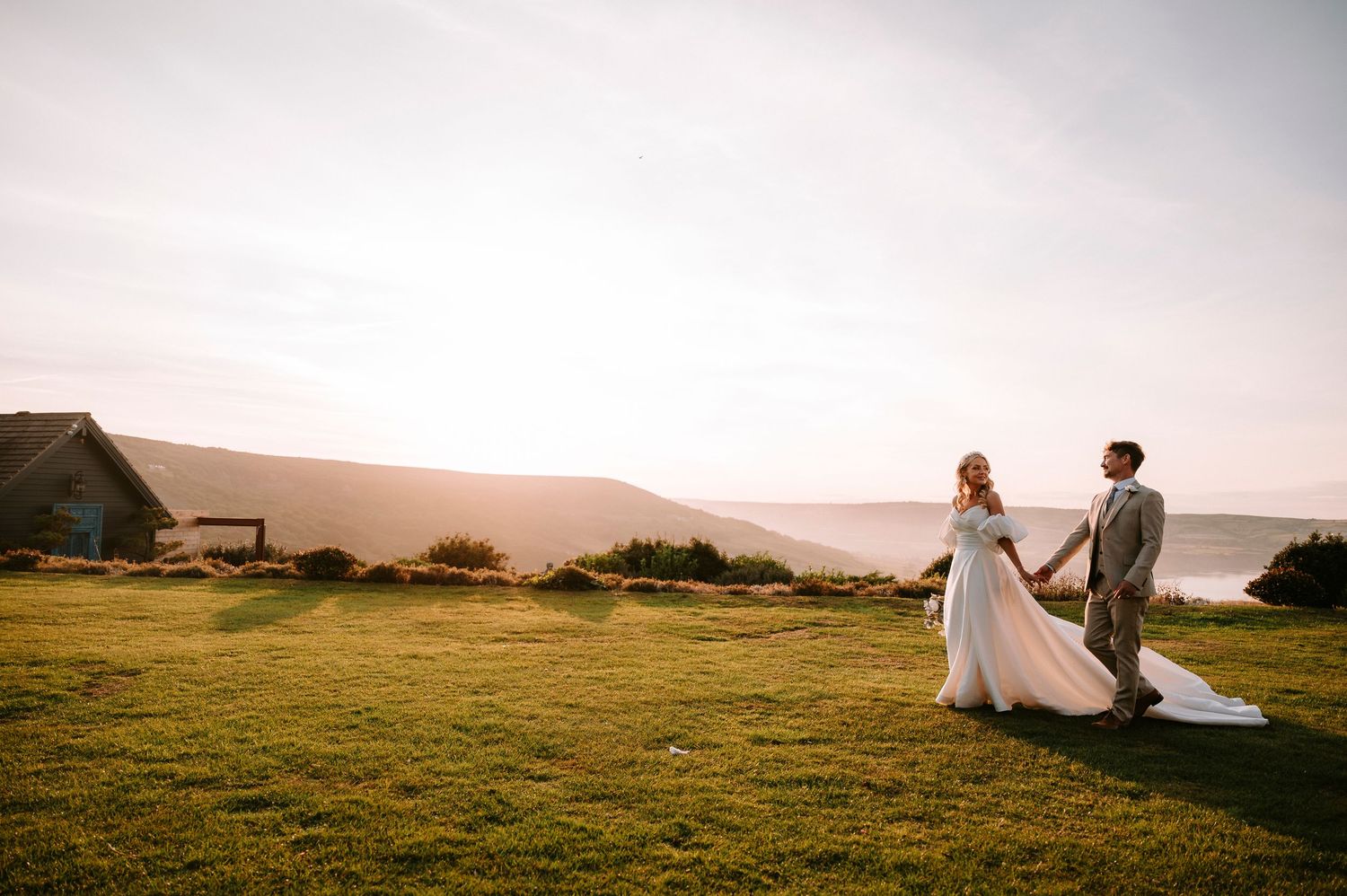Romantic coastal wedding photos captured during golden hour on a grassy cliff overlooking the ocean.