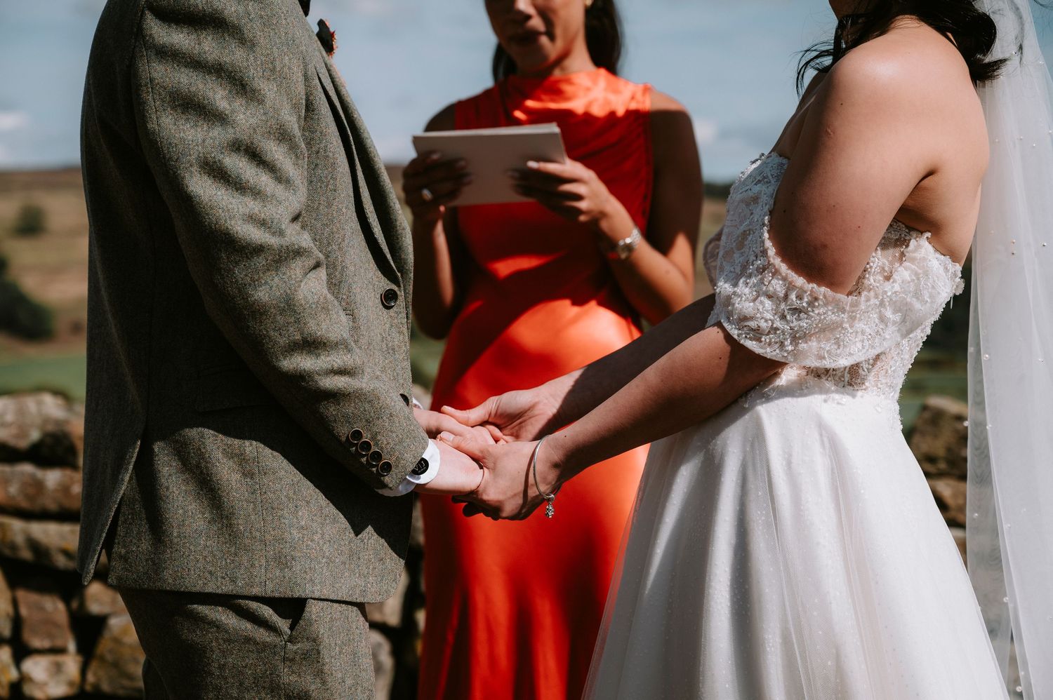 Wedding party gathered under rustic wooden arch with bright red fabric accents during outdoor ceremony.