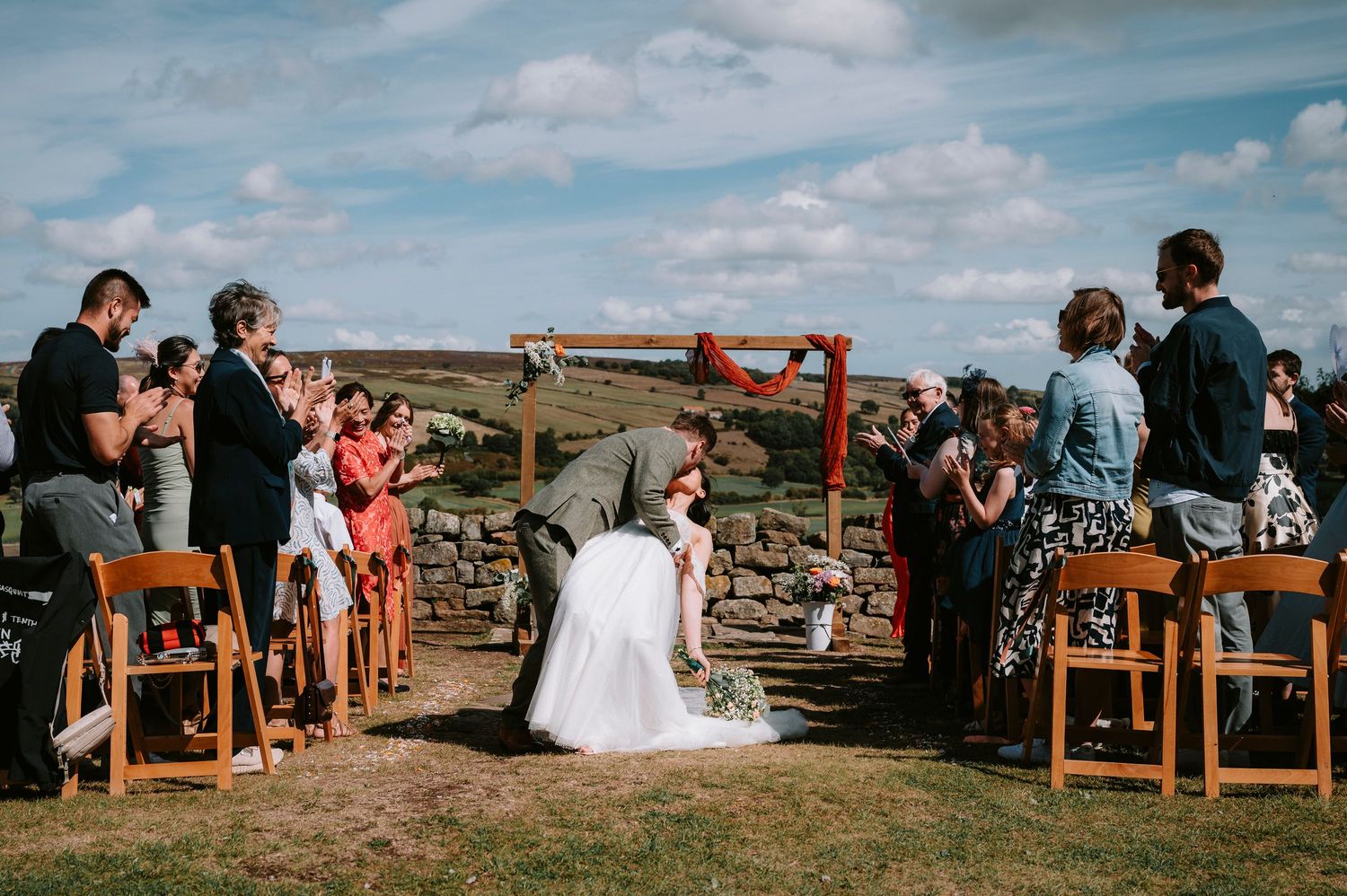 Wedding guests seated on wooden chairs at an outdoor ceremony with mountain views.