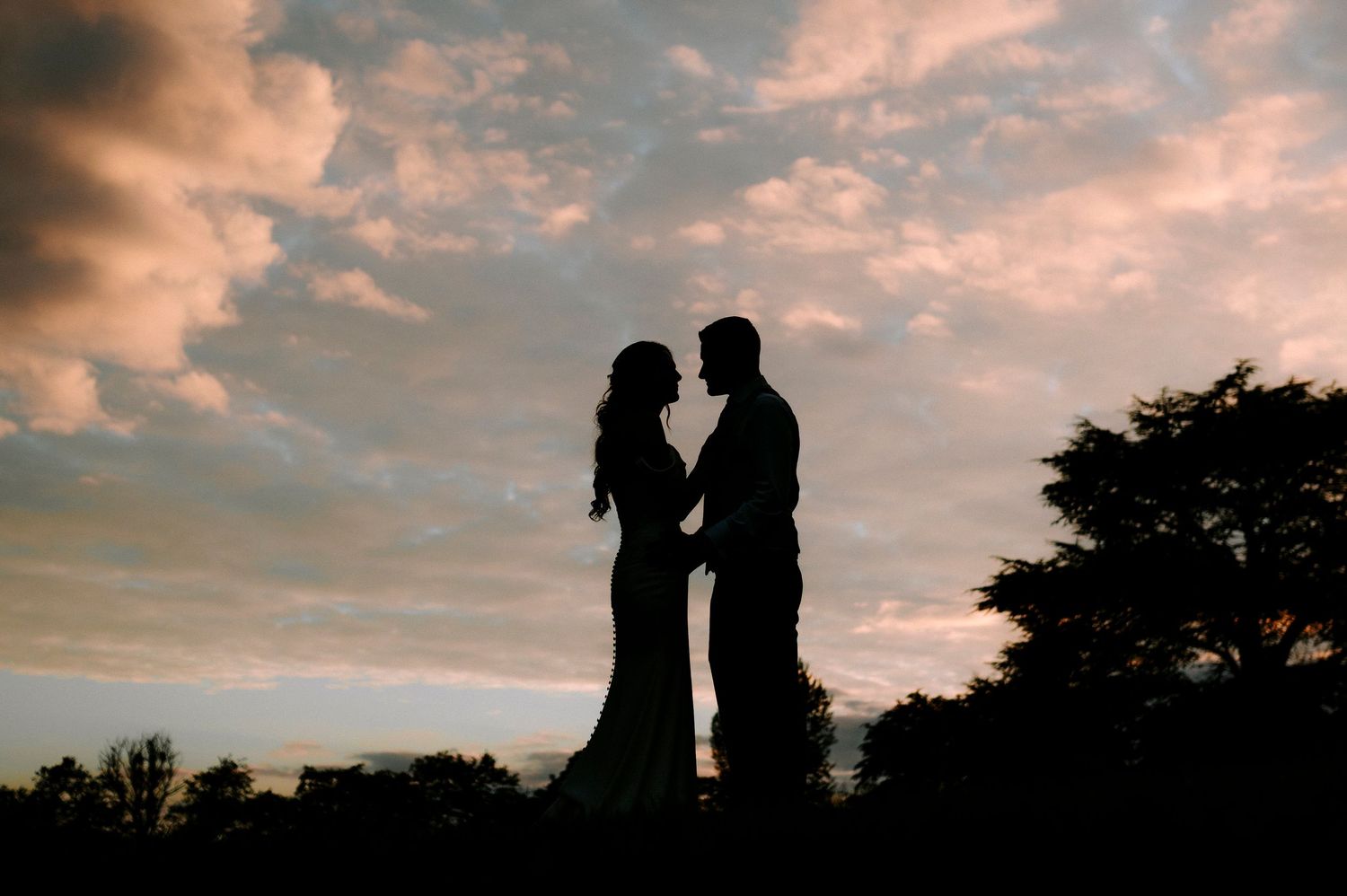 Two figures in silhouette share an intimate moment against a colorful dusk sky.