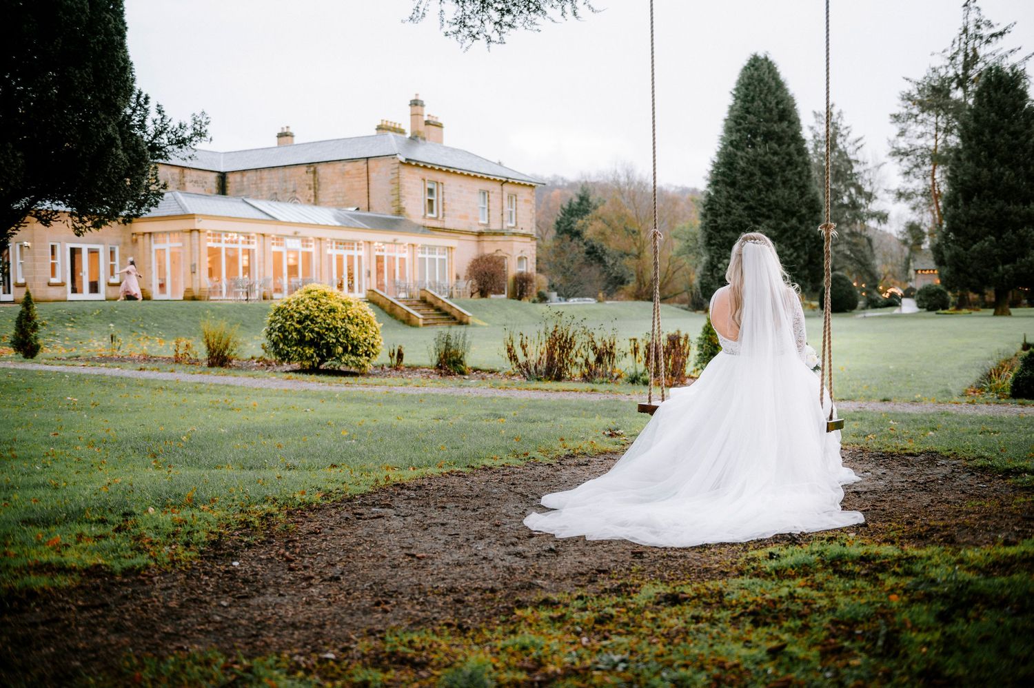 A bride's flowing white dress trails behind as she walks toward a grand country estate.