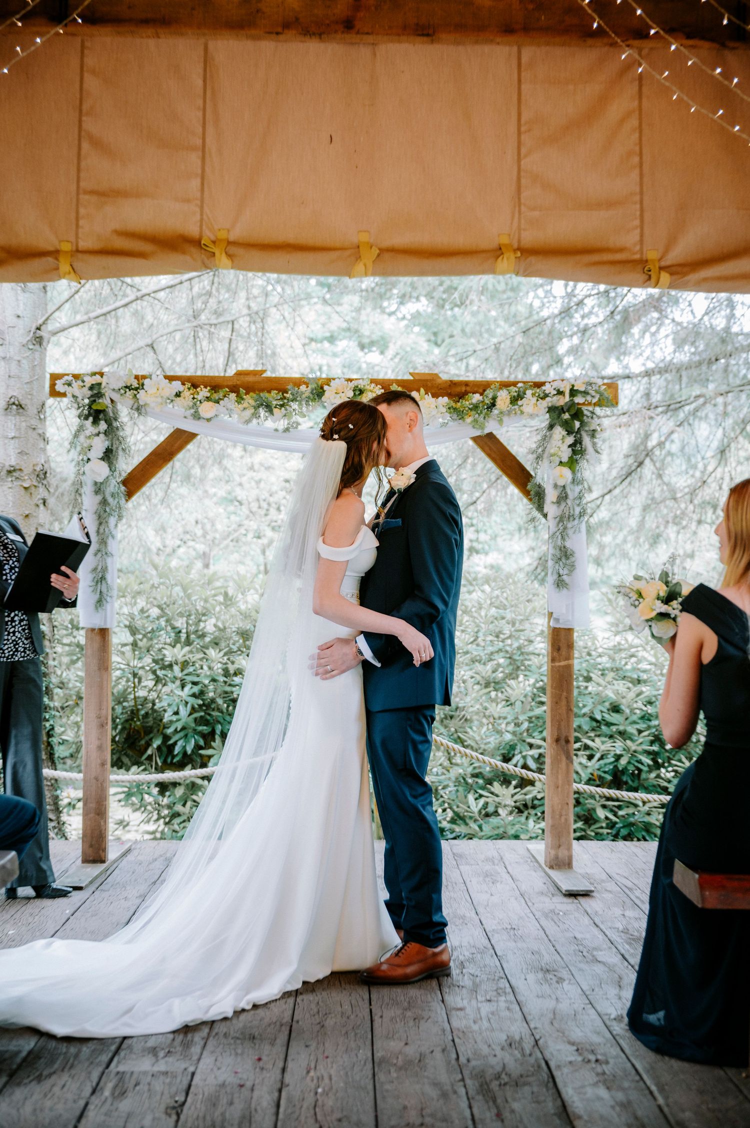 Wedding ceremony under wooden pavilion with romantic string lights and natural surroundings.