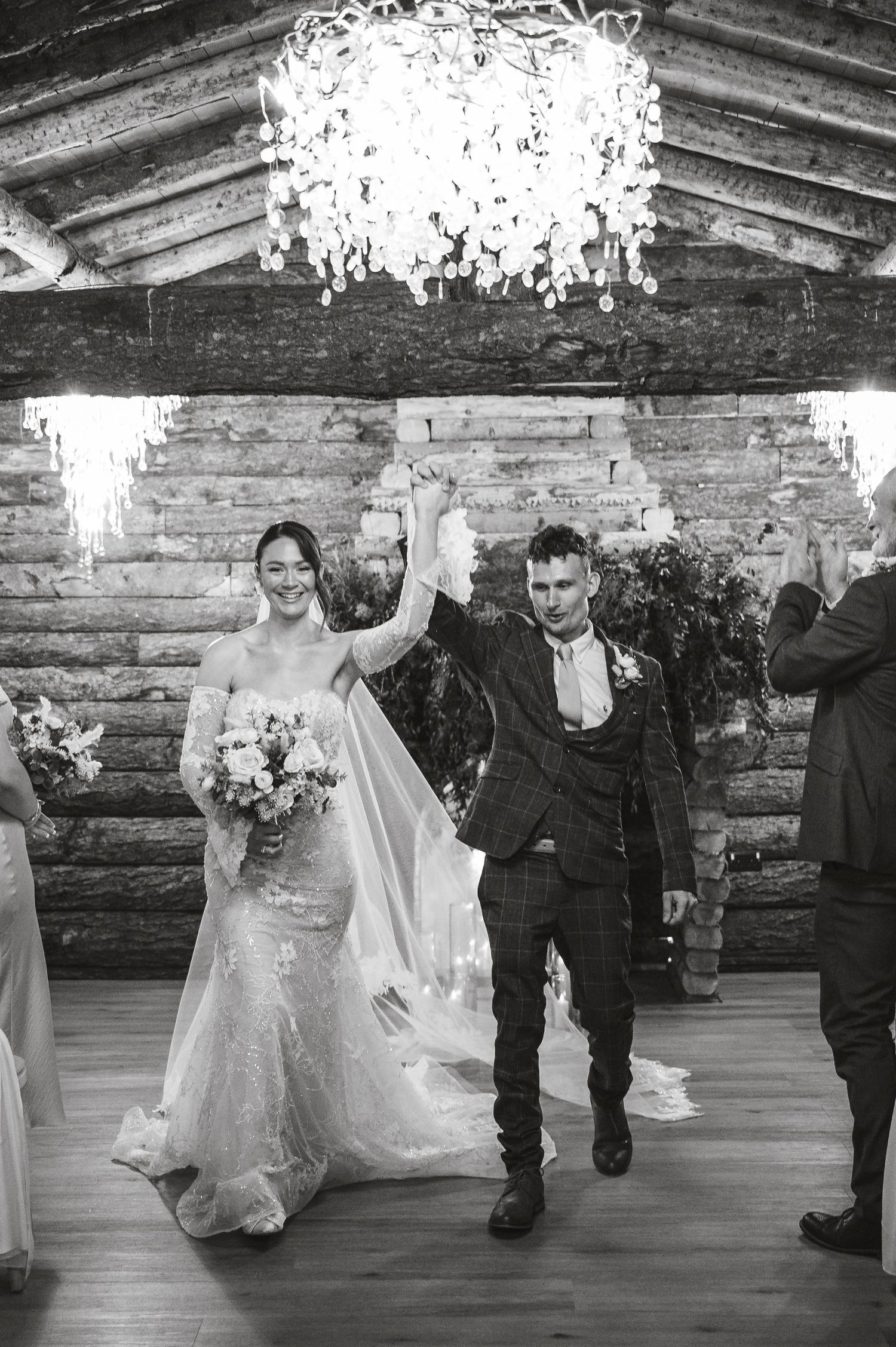 Wedding party celebrates in a rustic log cabin venue with string lights overhead during reception.